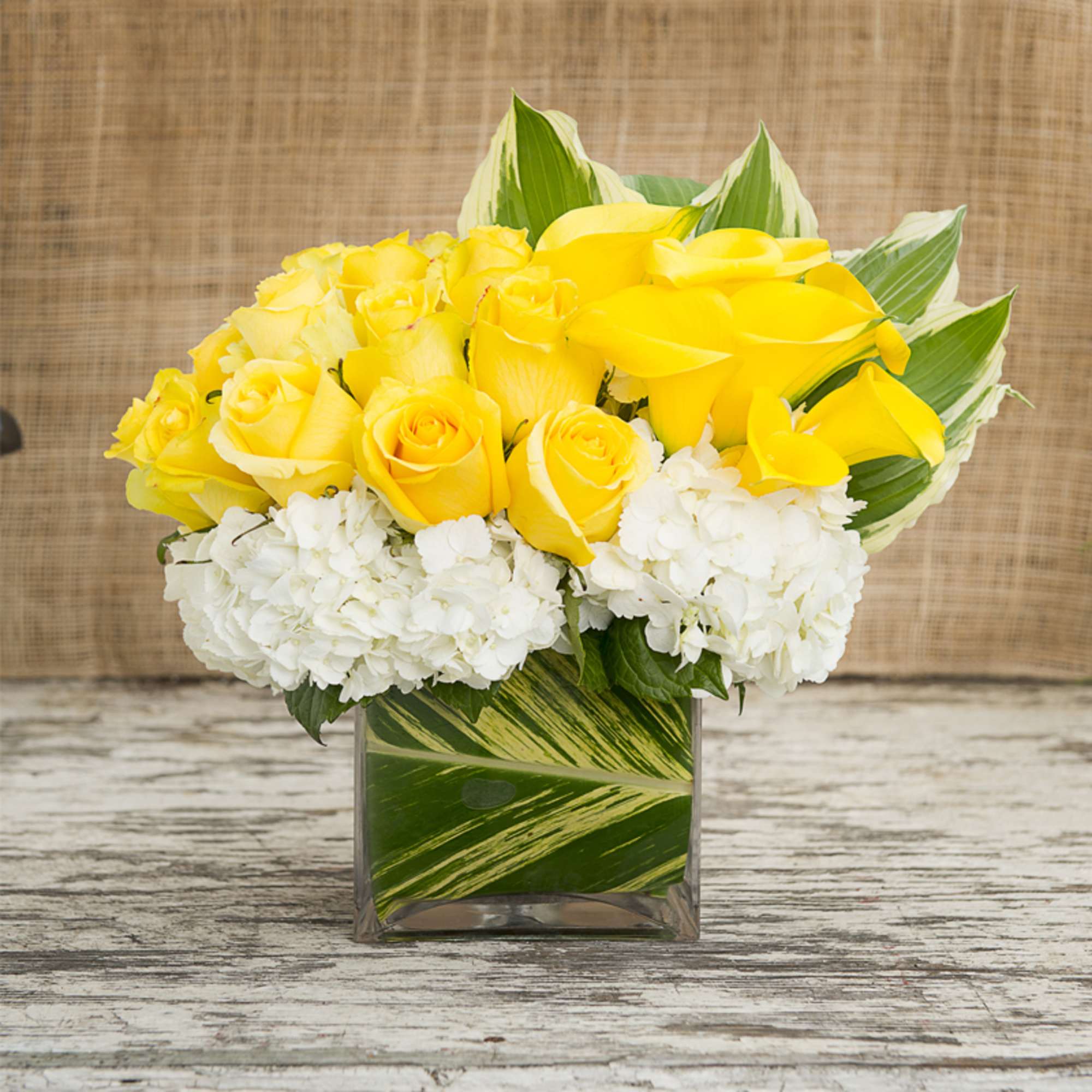 Yellow roses and white hydrangeas in a square glass vase