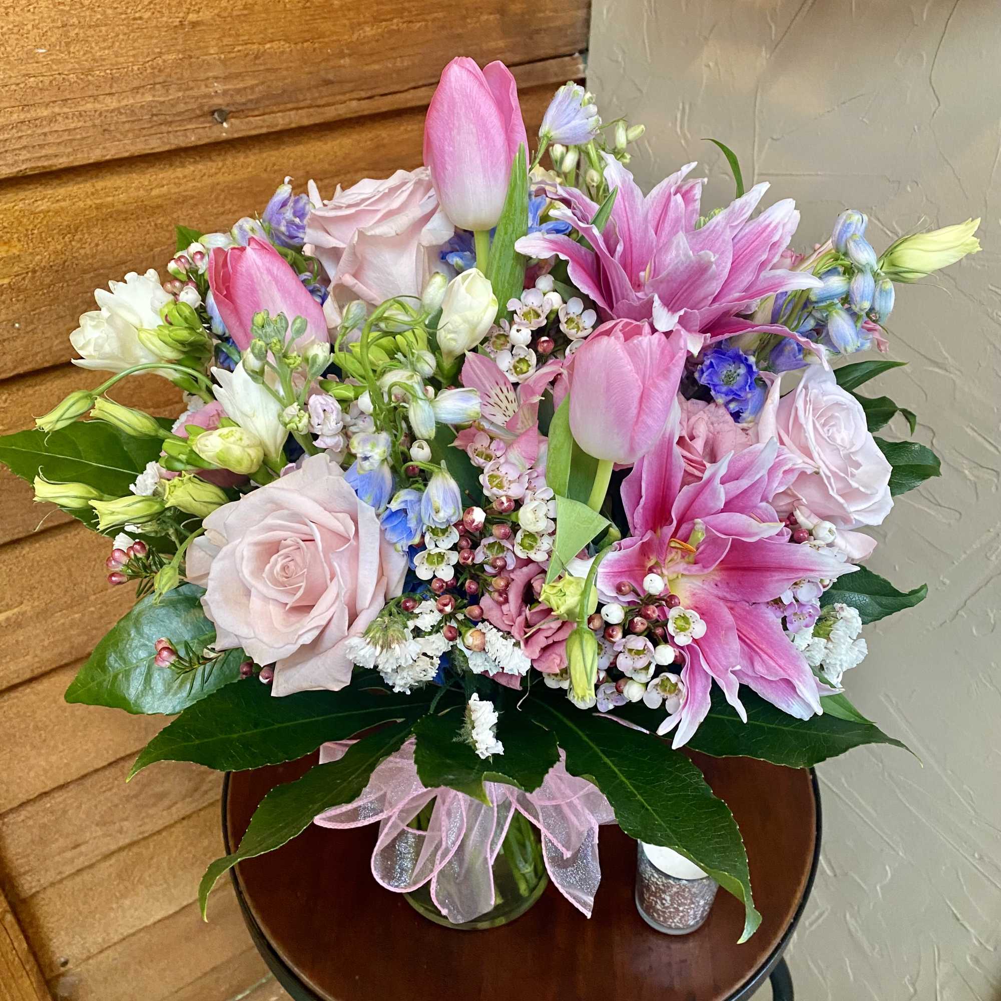 Pink tulips and lilies arranged with pale roses in a glass vase