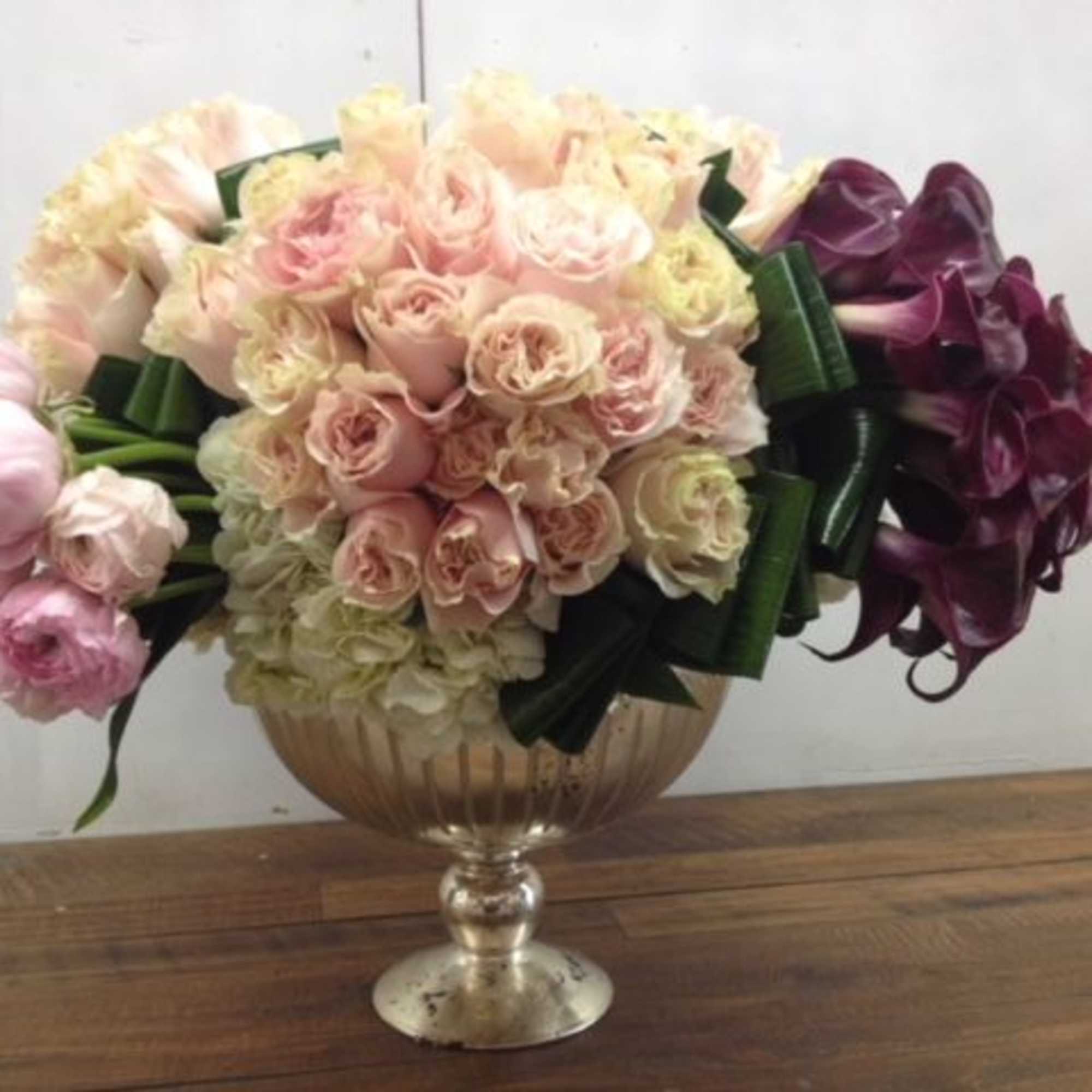 Bouquet of pale pink and cream roses in a glass vase with dark purple flowers