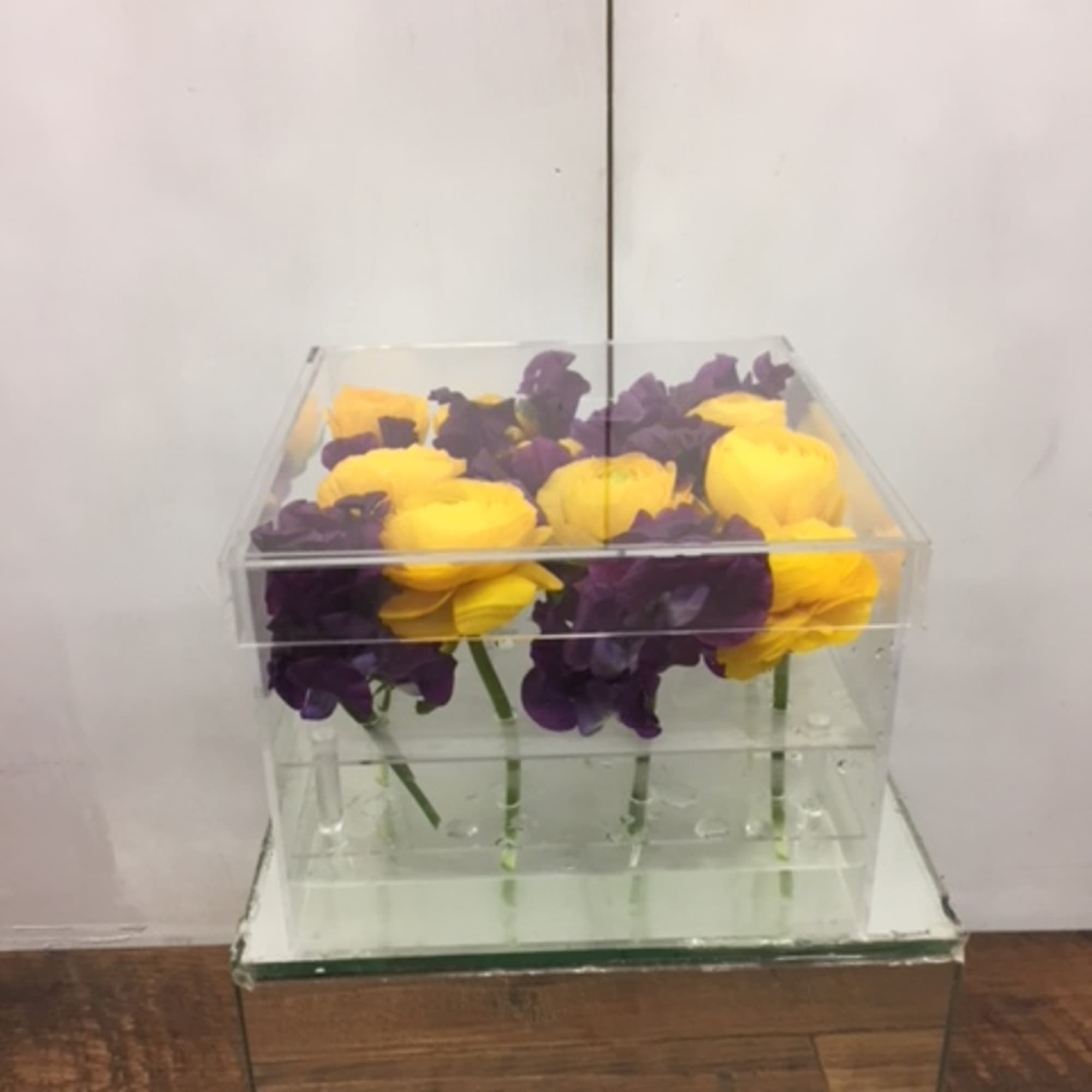 Yellow and purple flowers arranged in a clear acrylic box
