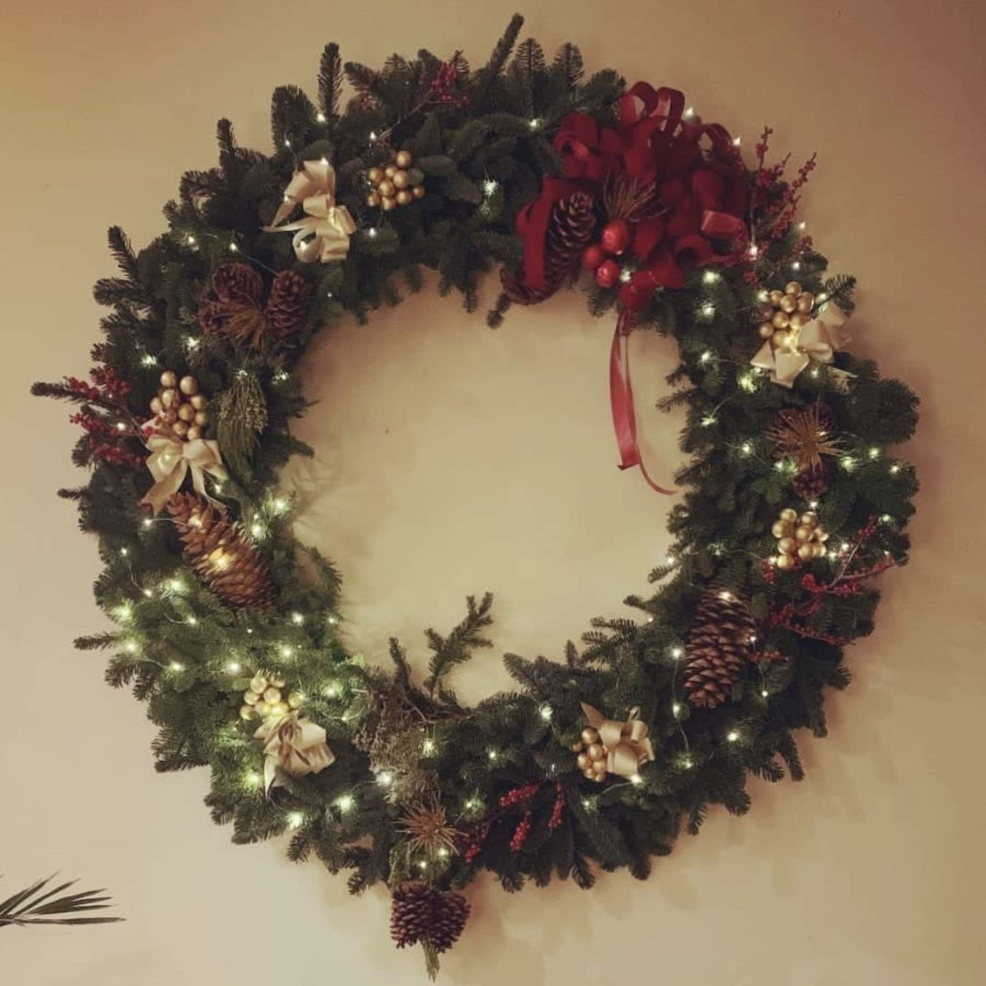 Decorated evergreen wreath with lights, pinecones, bows, and red accents