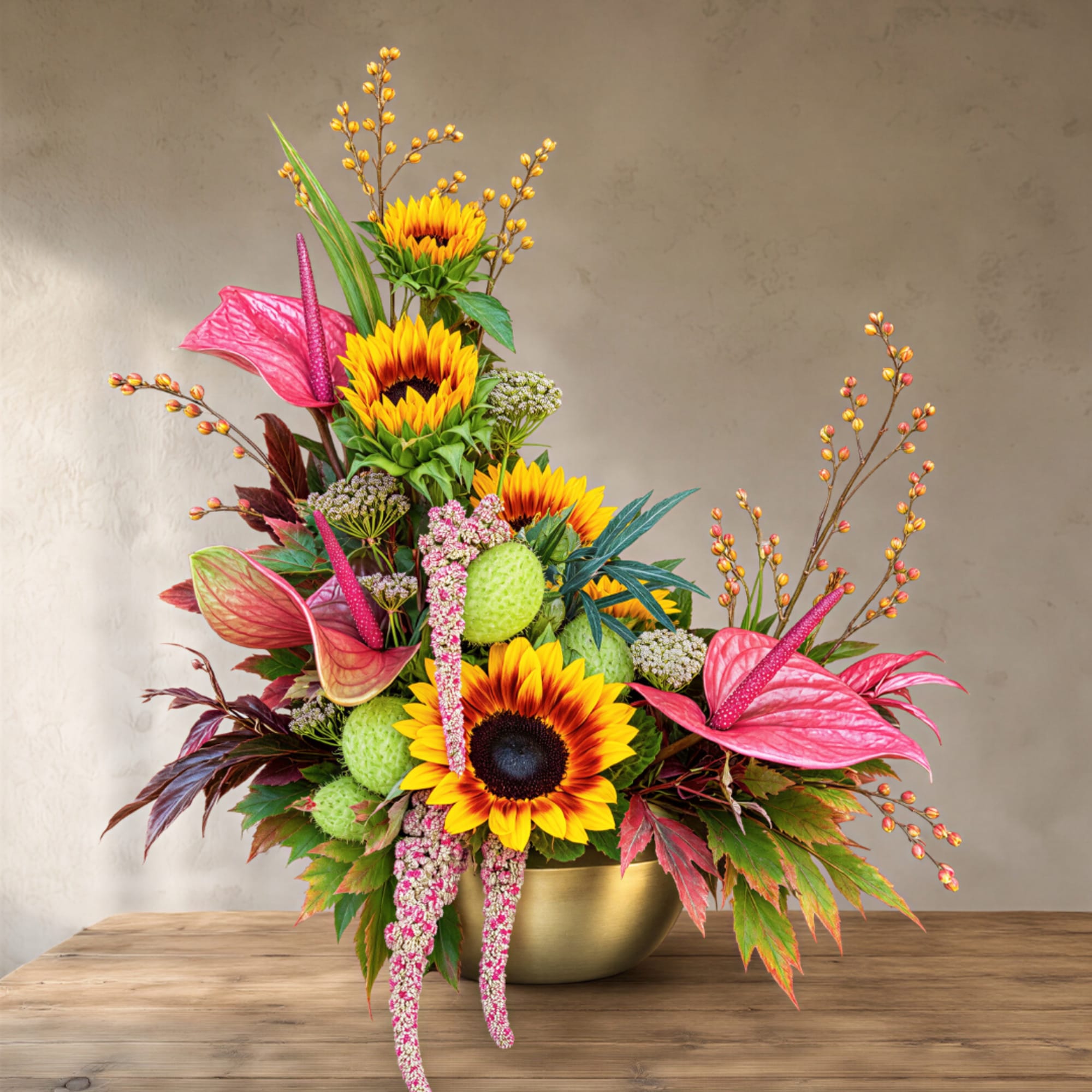 Sunflower arrangement in a gold bowl with pink anthuriums and berries