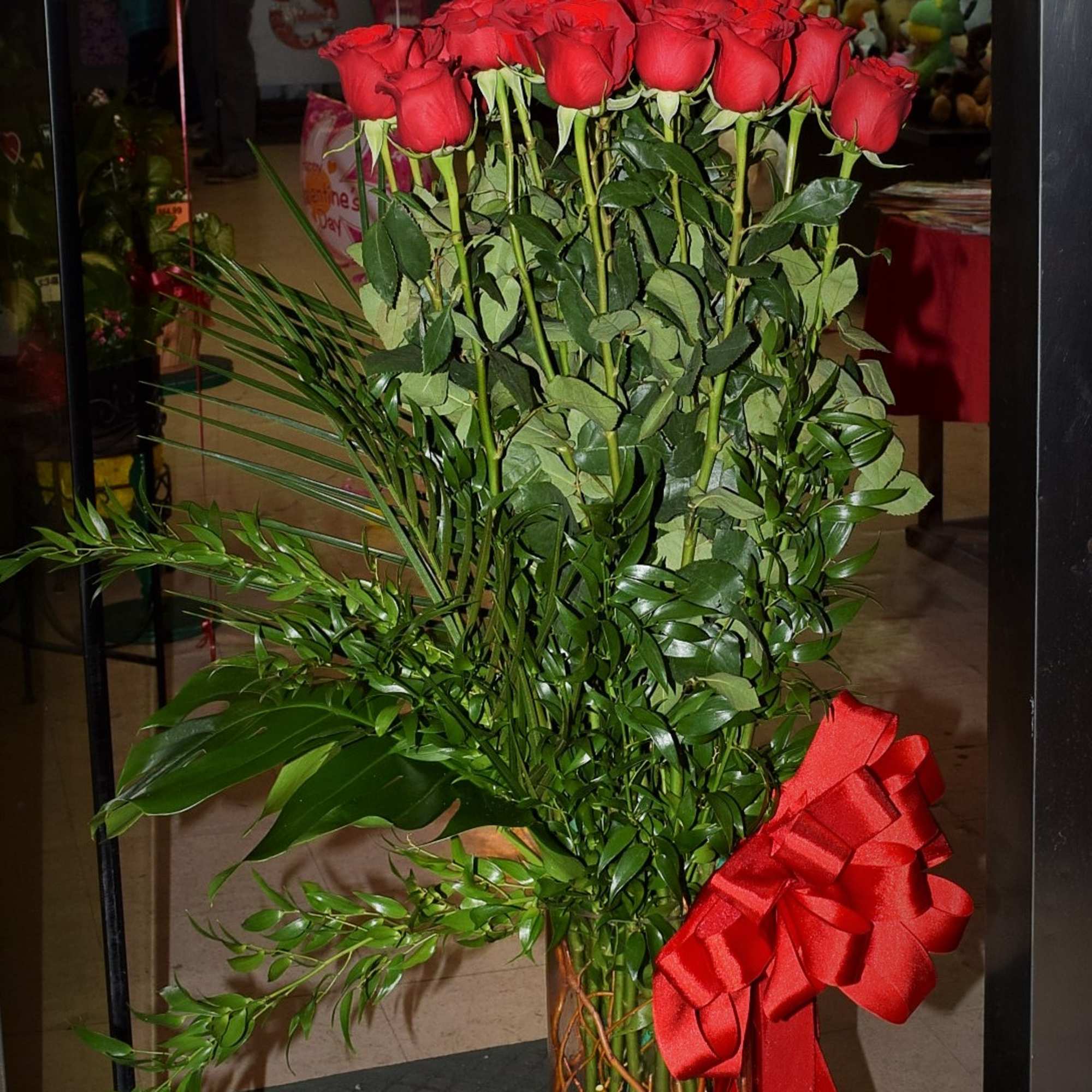 Tall bouquet of red roses in a glass vase with a red ribbon
