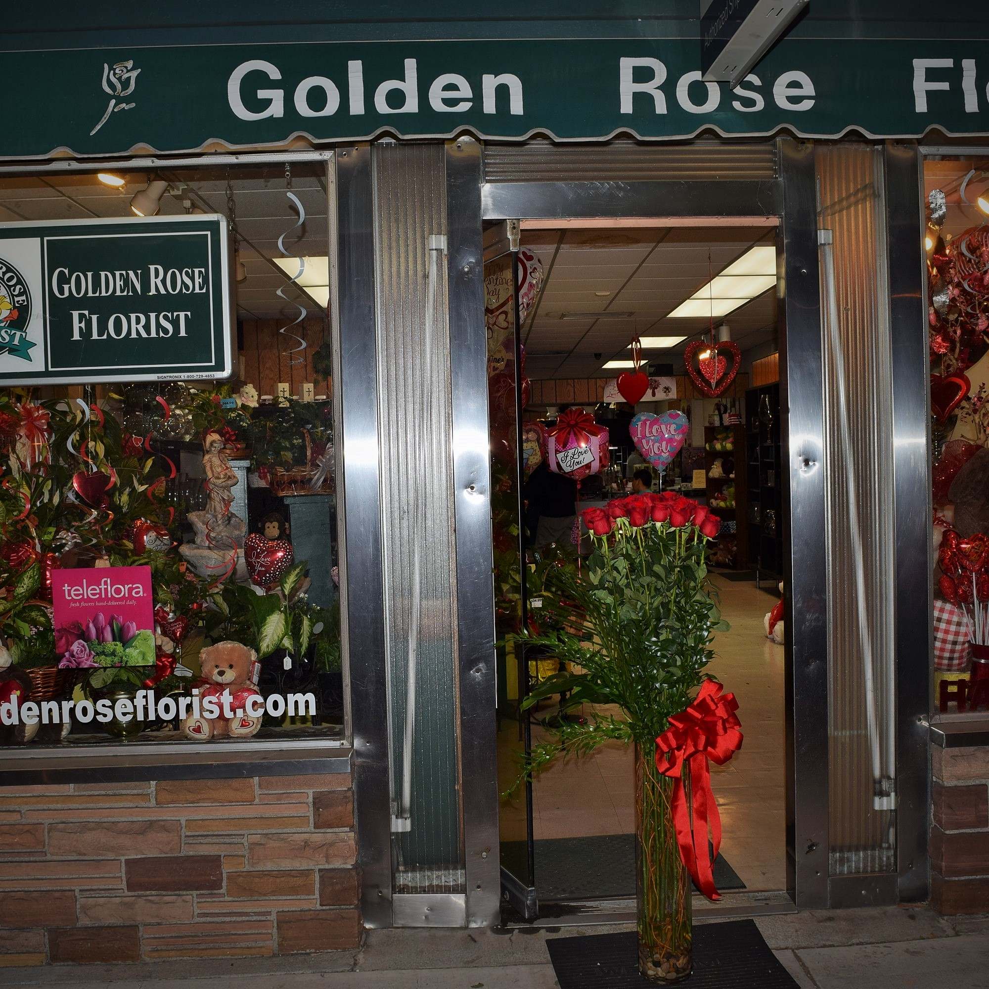Florist storefront with a tall vase of red roses at the entrance
