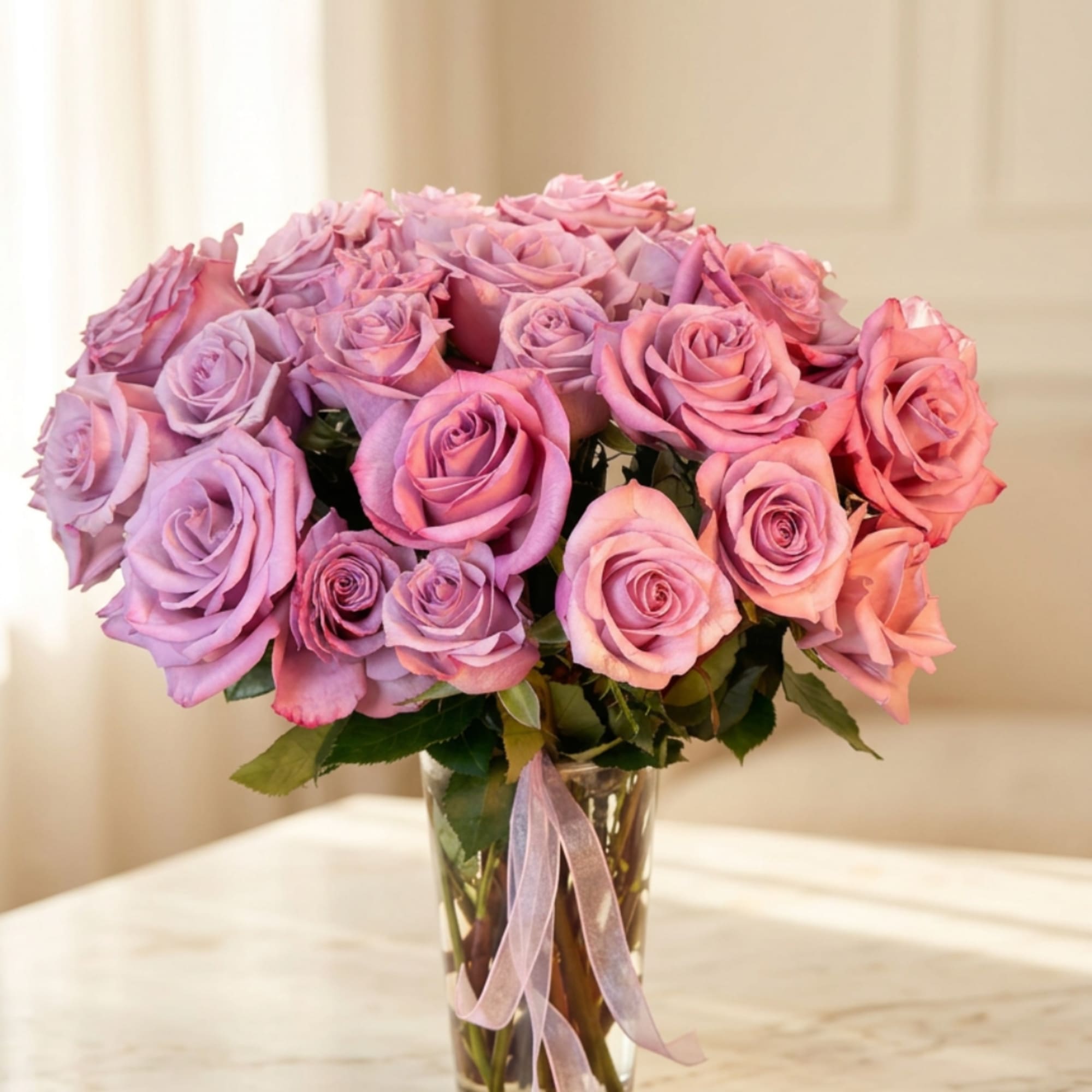 Pink and lavender roses in a clear glass vase with a ribbon