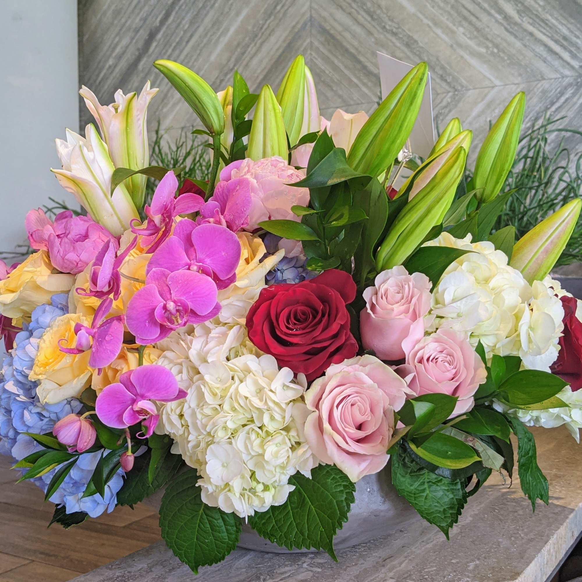 Mixed bouquet of roses, lilies, orchids, and hydrangeas in a low container