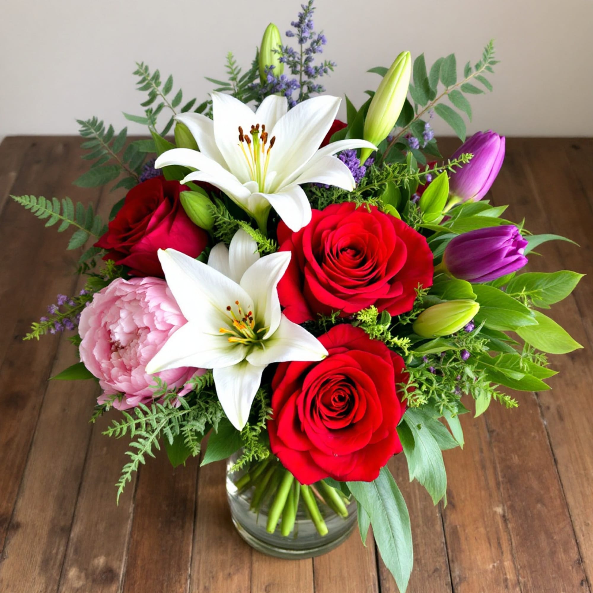 Bouquet of red roses, white lilies, and pink blooms in a glass vase