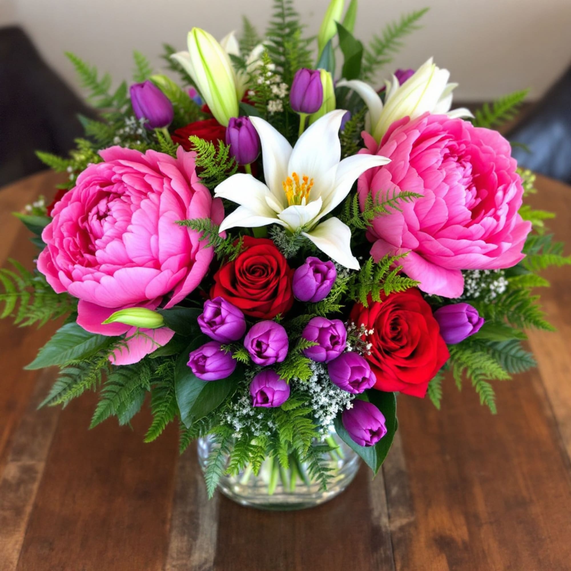 Pink peonies, red roses, and white lilies in a glass vase