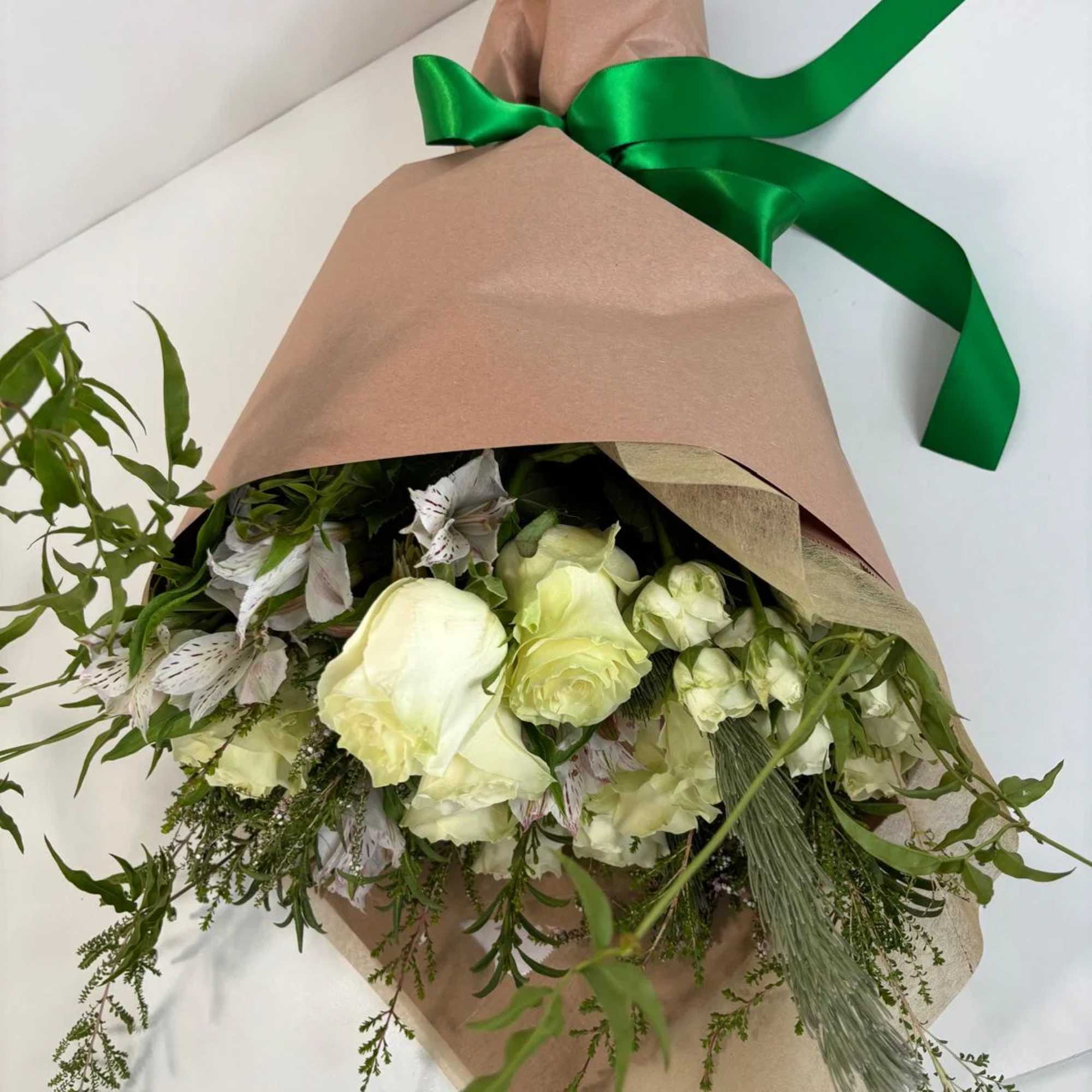 Wrapped bouquet of pale cream flowers with a green ribbon