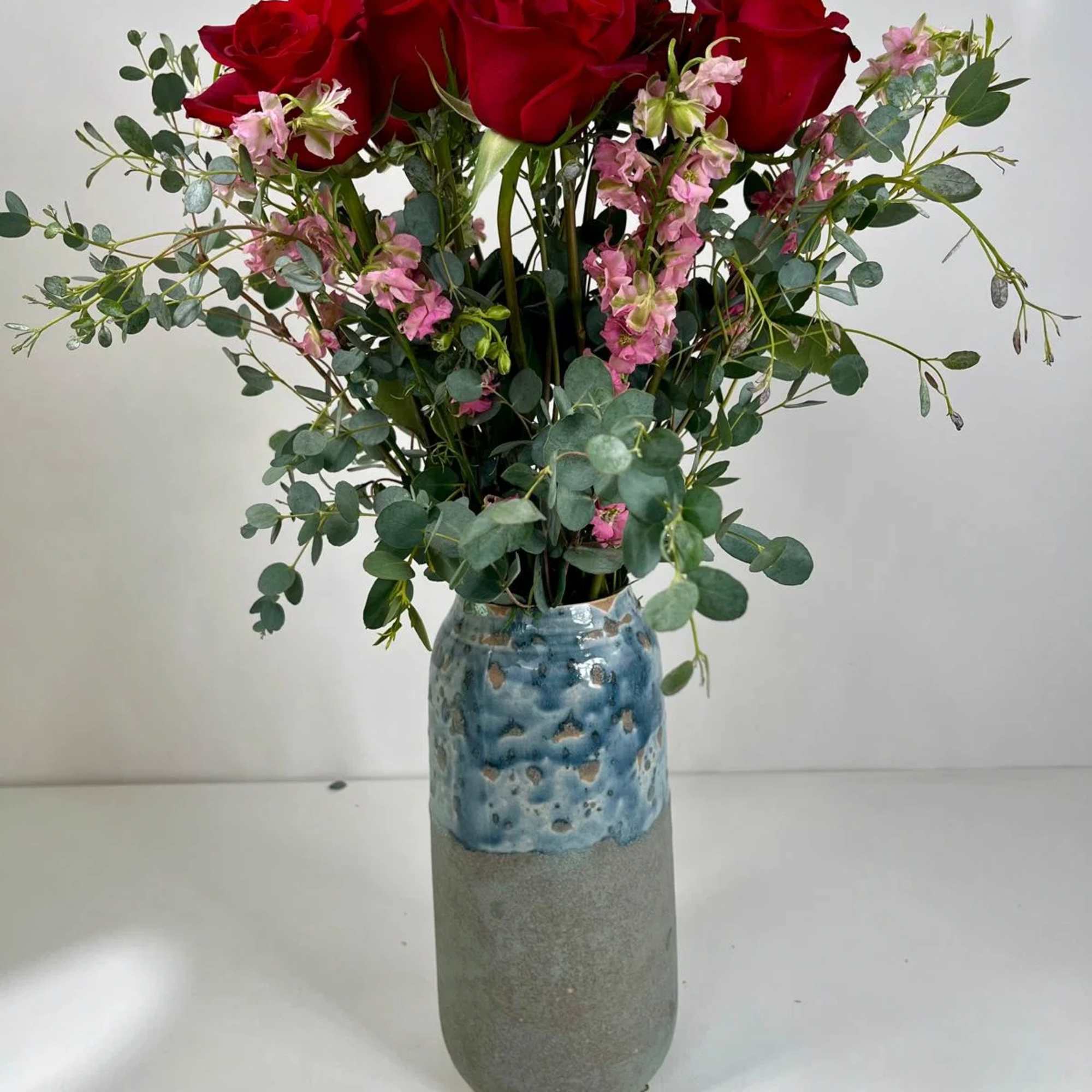 Red roses with pink filler flowers in a tall ceramic vase