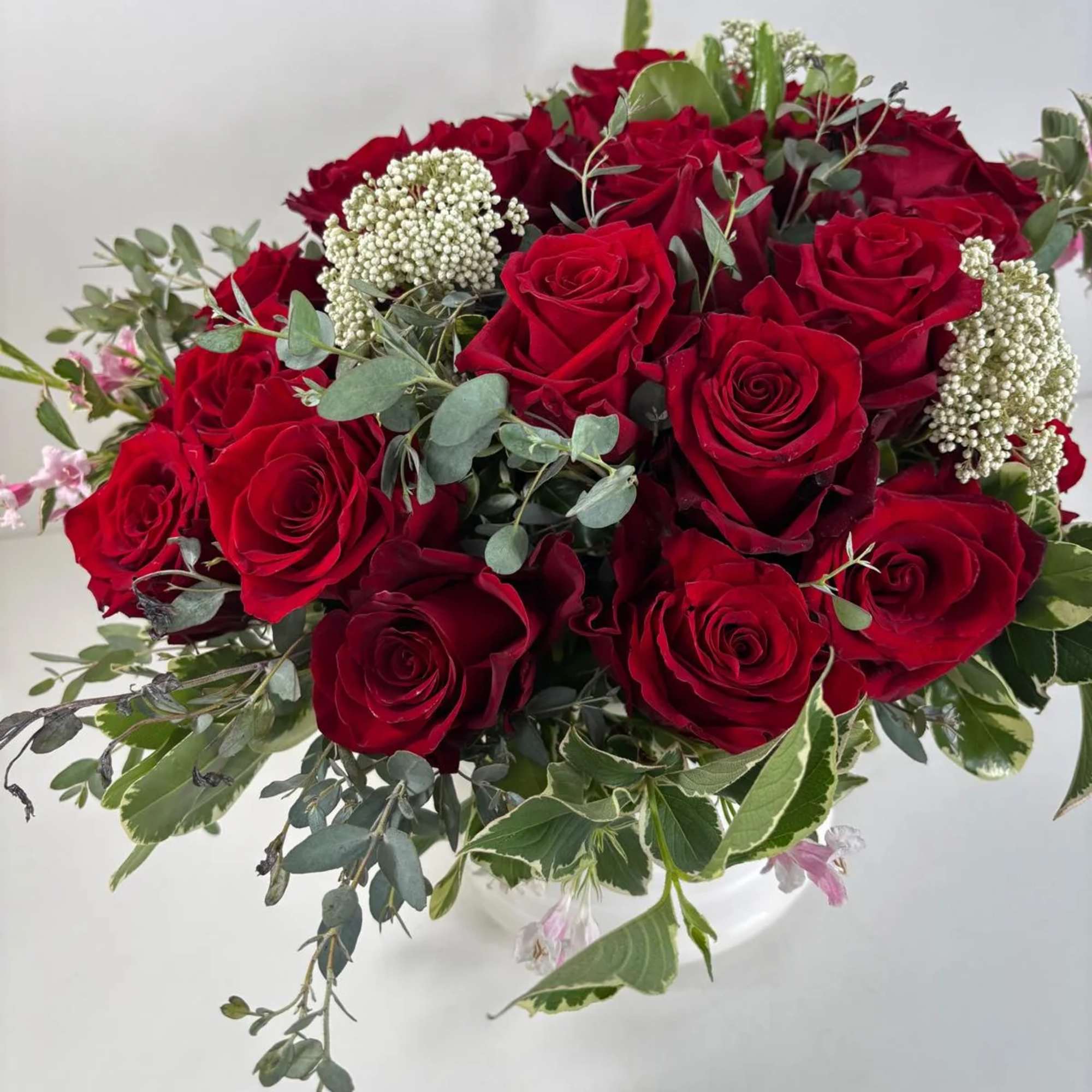 Bouquet of red roses with mixed greenery and white filler flowers in a white vase