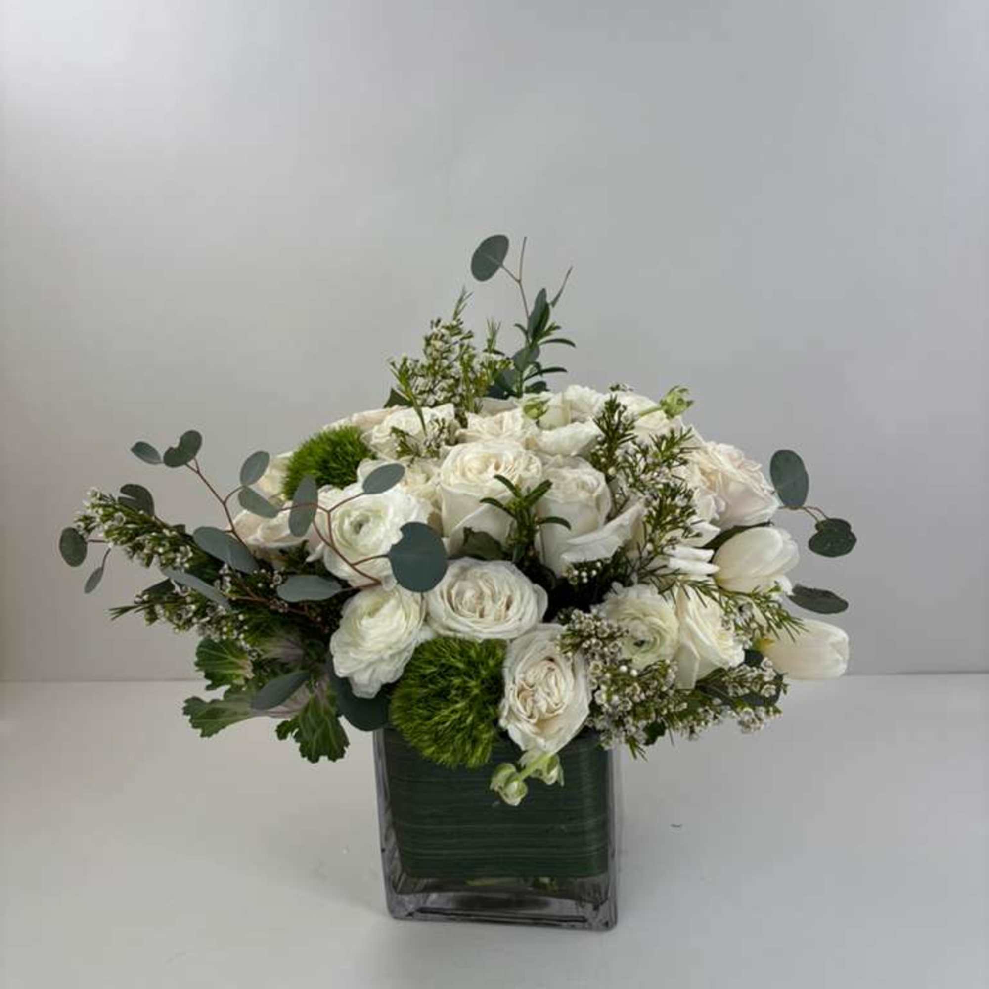 White floral arrangement in a square glass vase with eucalyptus accents
