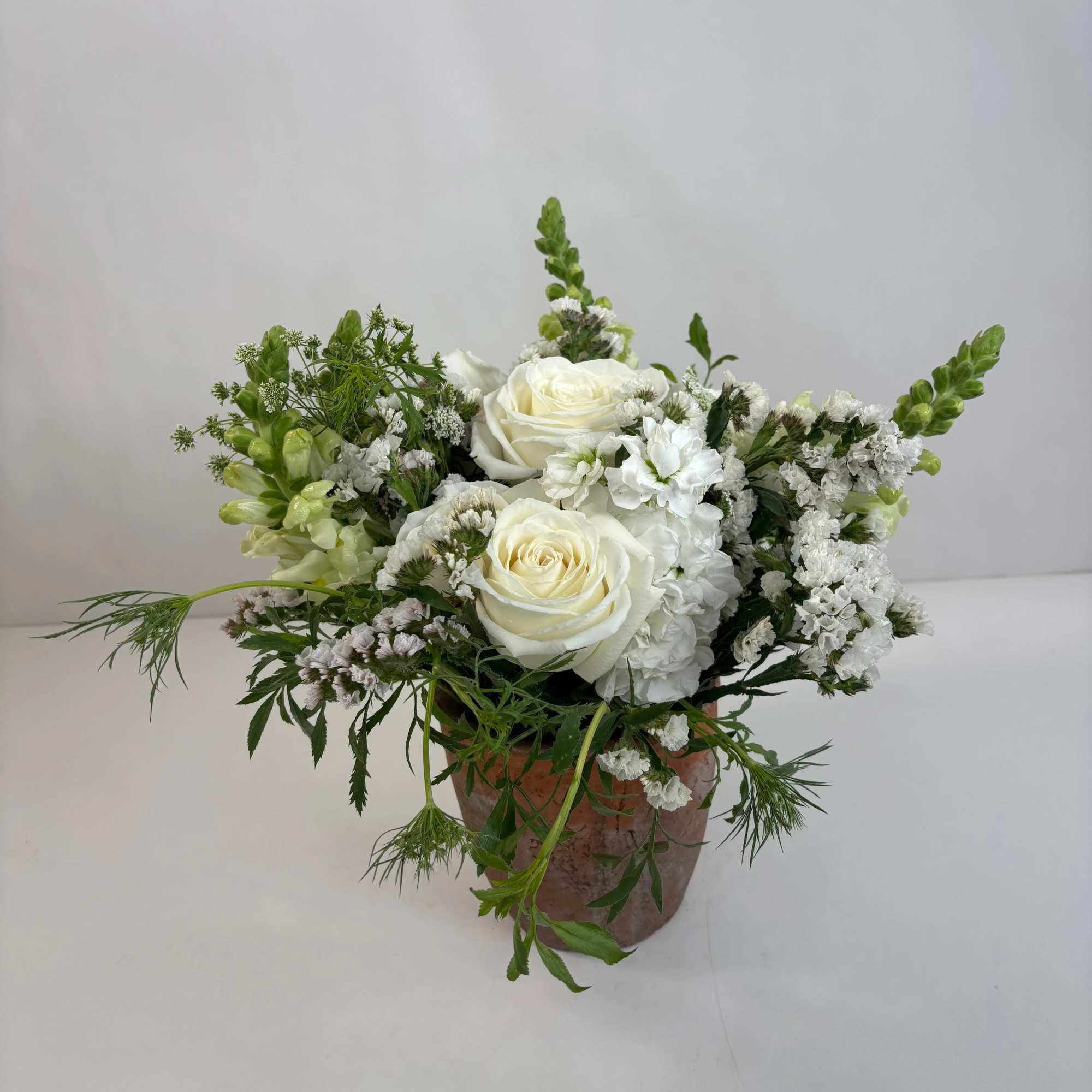 White roses and white filler flowers arranged in a rustic pot