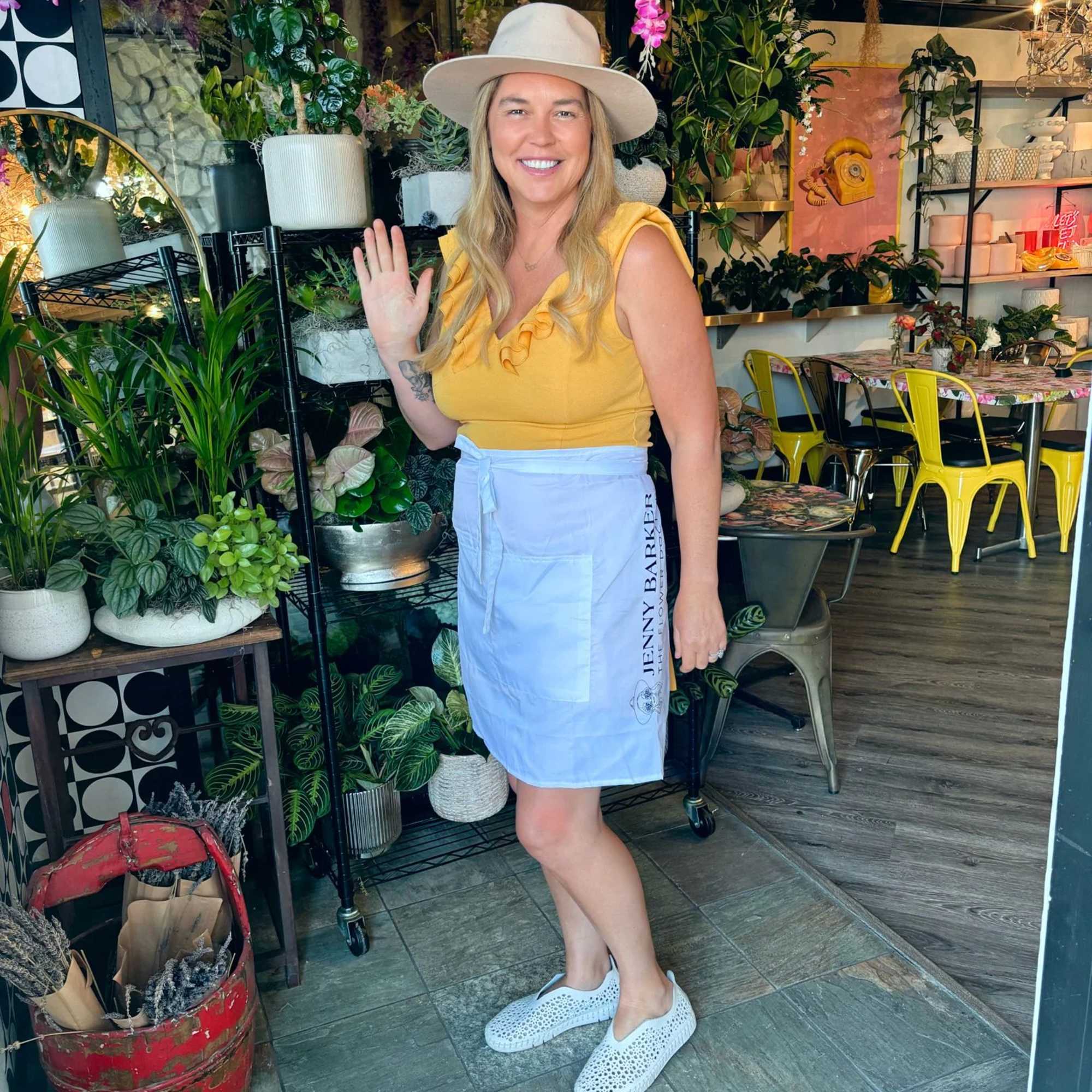 Woman standing in a plant shop with hanging pink flowers and potted greenery