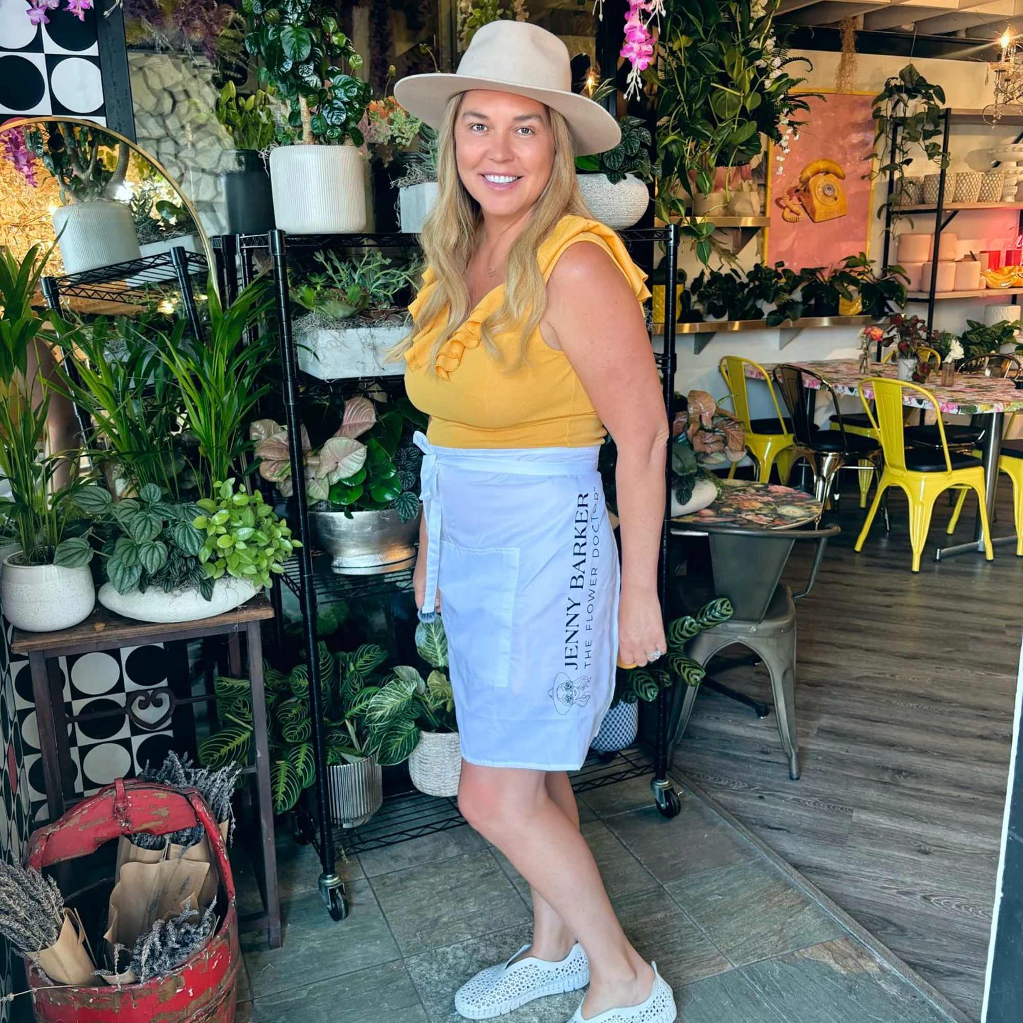 Woman standing in a flower shop with hanging pink orchids and potted plants