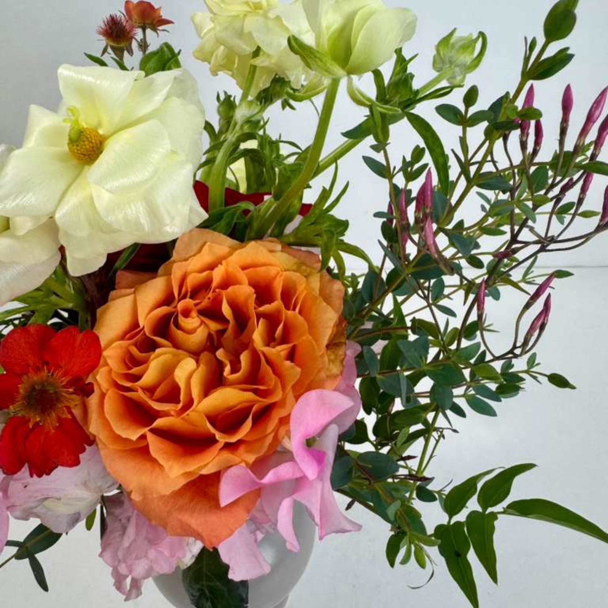 Bouquet with orange and white roses, pink blooms, and greenery in a vase