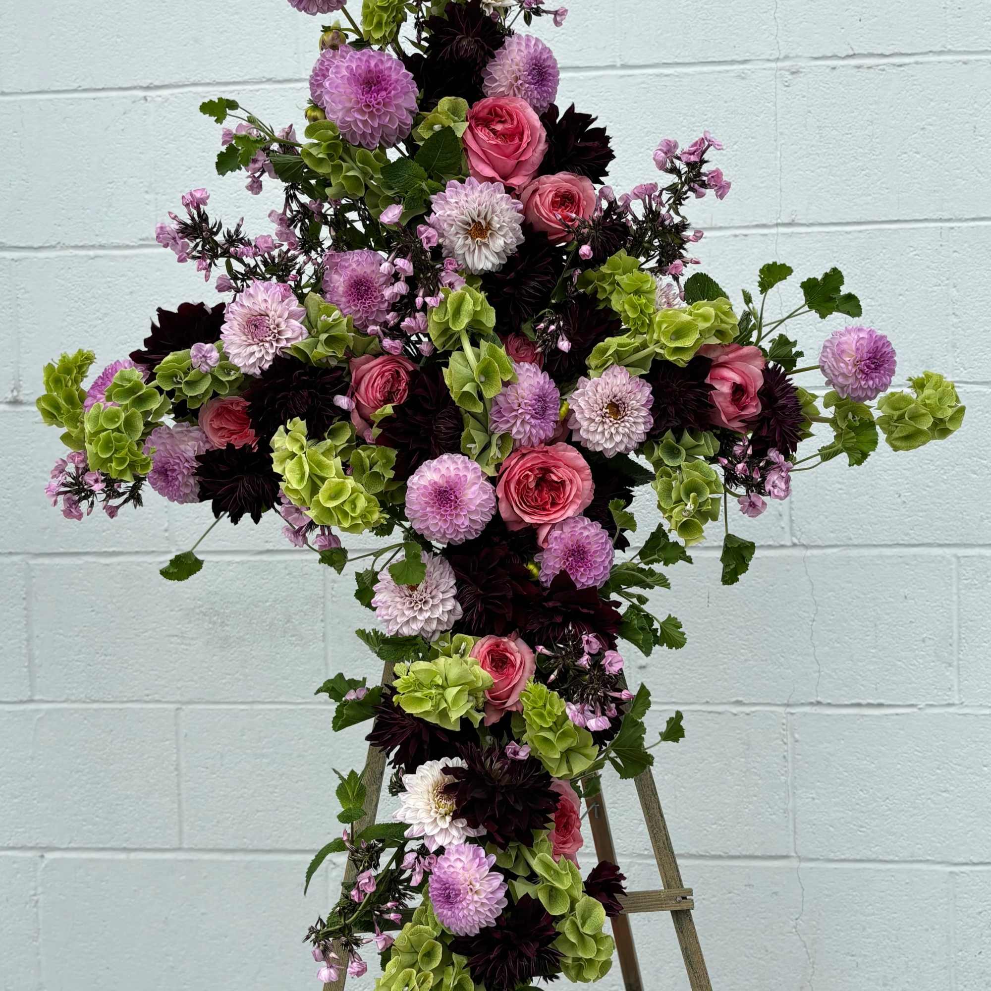 Cross-shaped floral arrangement with pink, purple, white, and green blooms