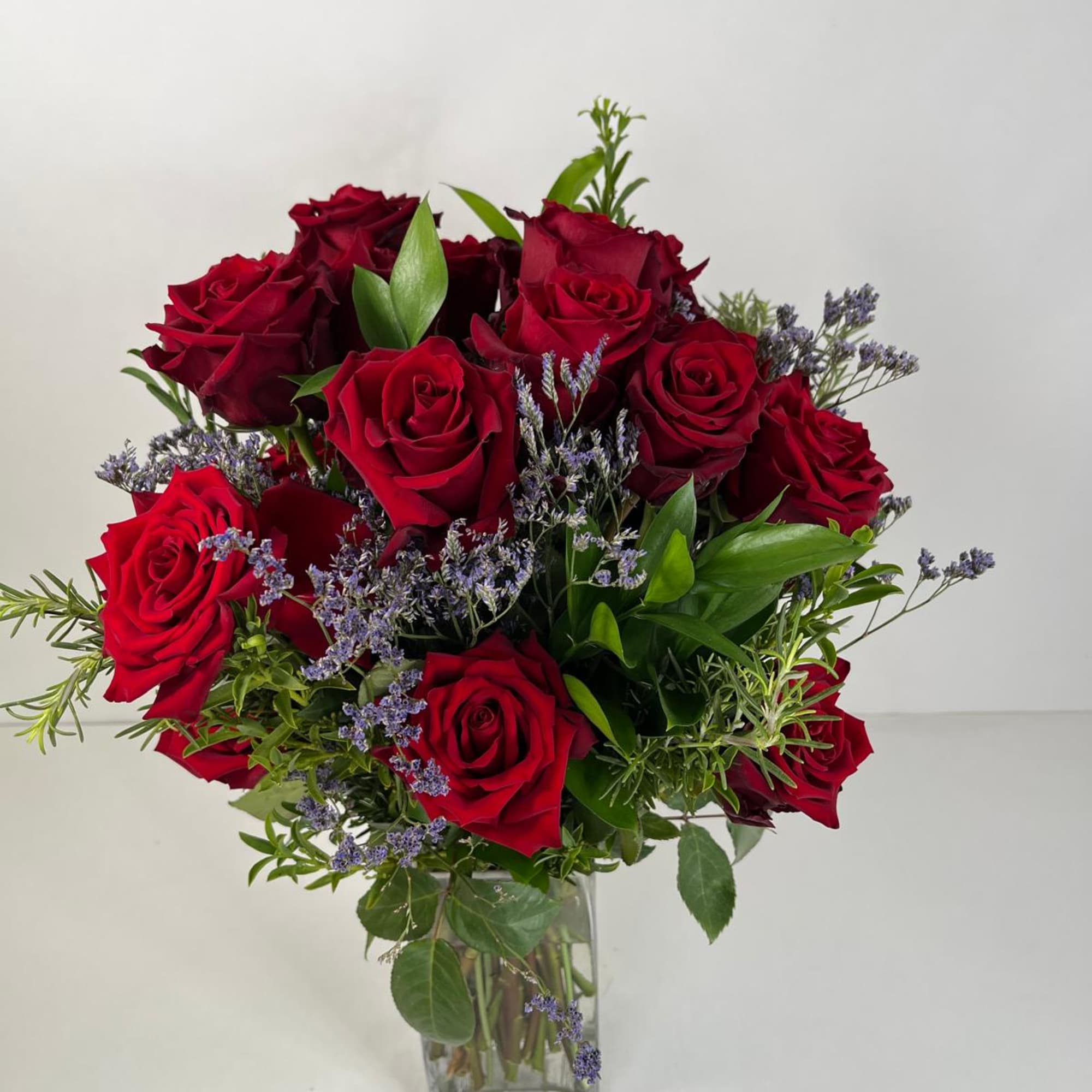 Red roses arranged in a clear glass vase with purple filler flowers, photo 4 of 5