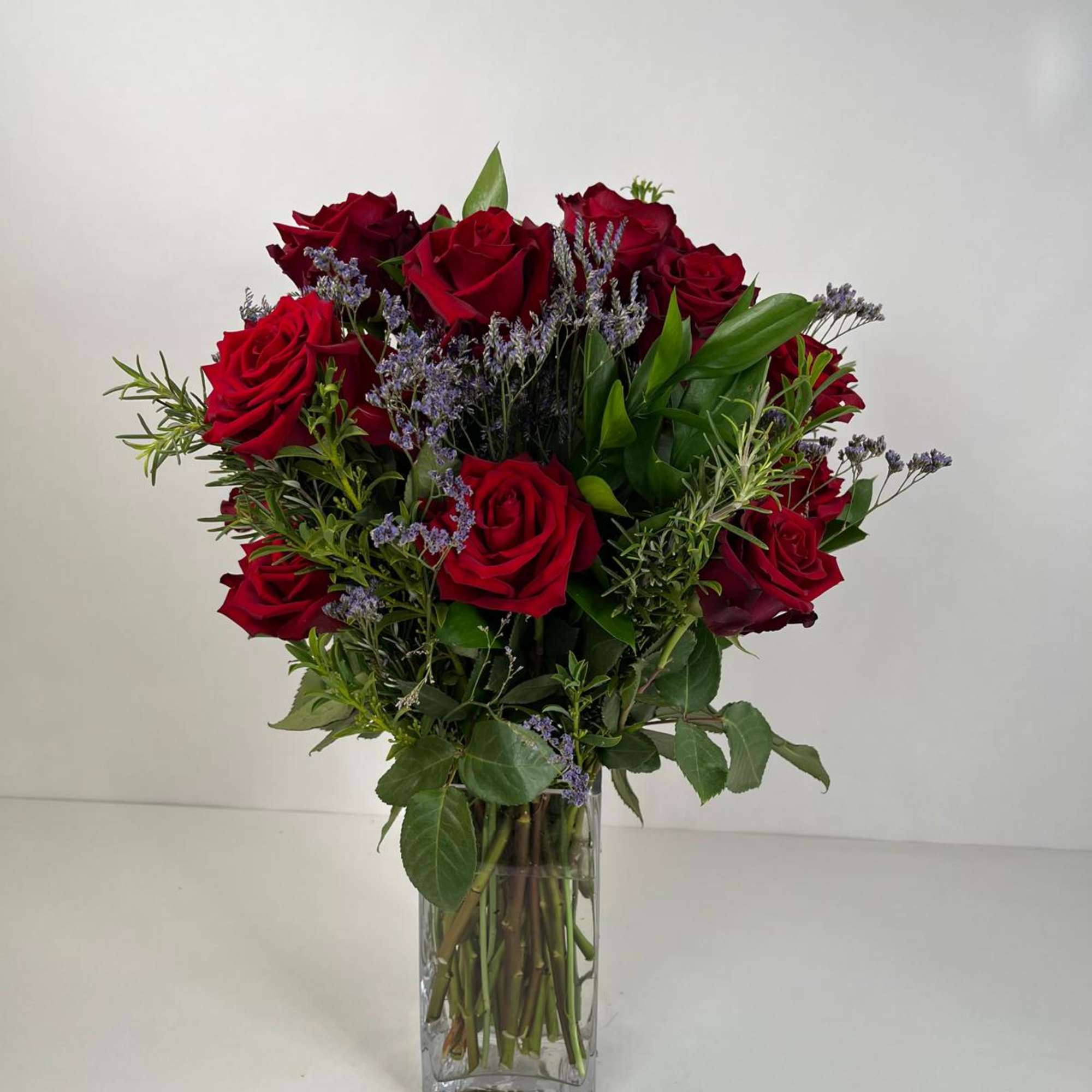 Red roses arranged in a clear glass vase with purple filler flowers, photo 2 of 5