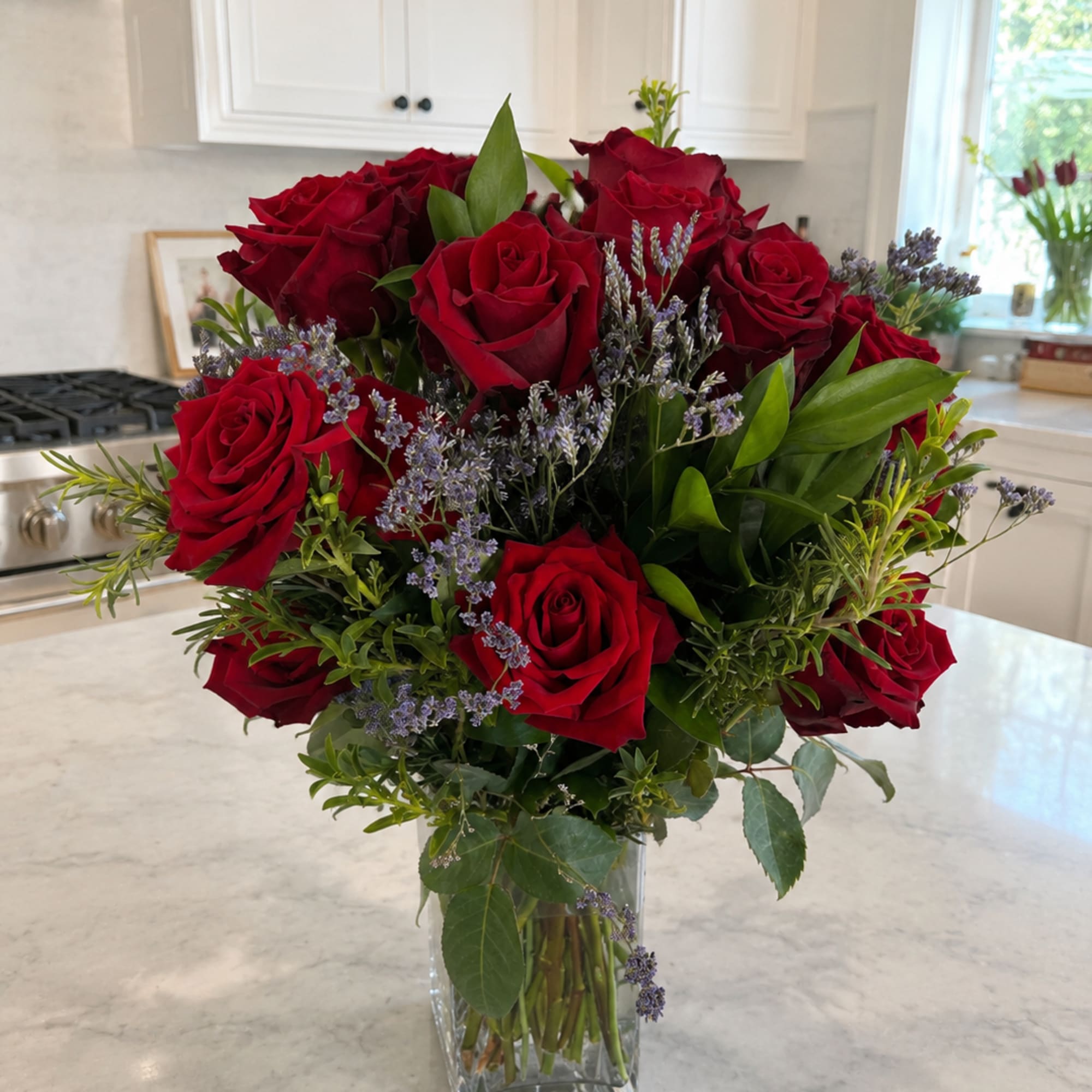 Red roses arranged in a clear glass vase with purple filler flowers.