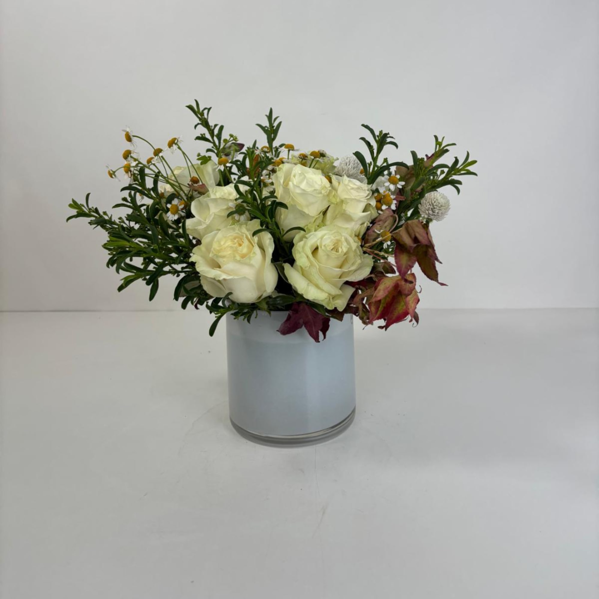 White roses in a glass vase with small accent flowers and foliage