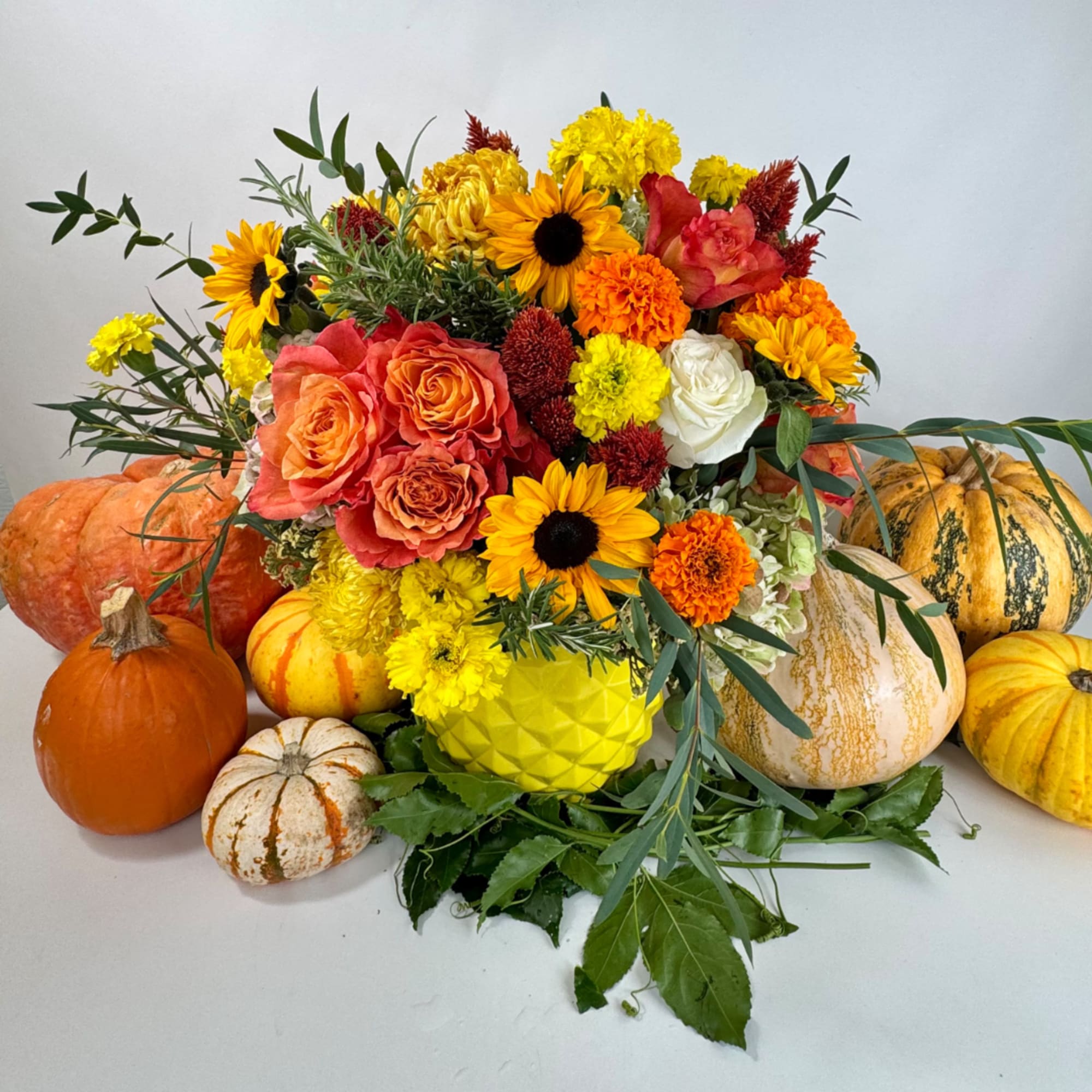 Autumn bouquet with sunflowers, roses, and mums surrounded by pumpkins