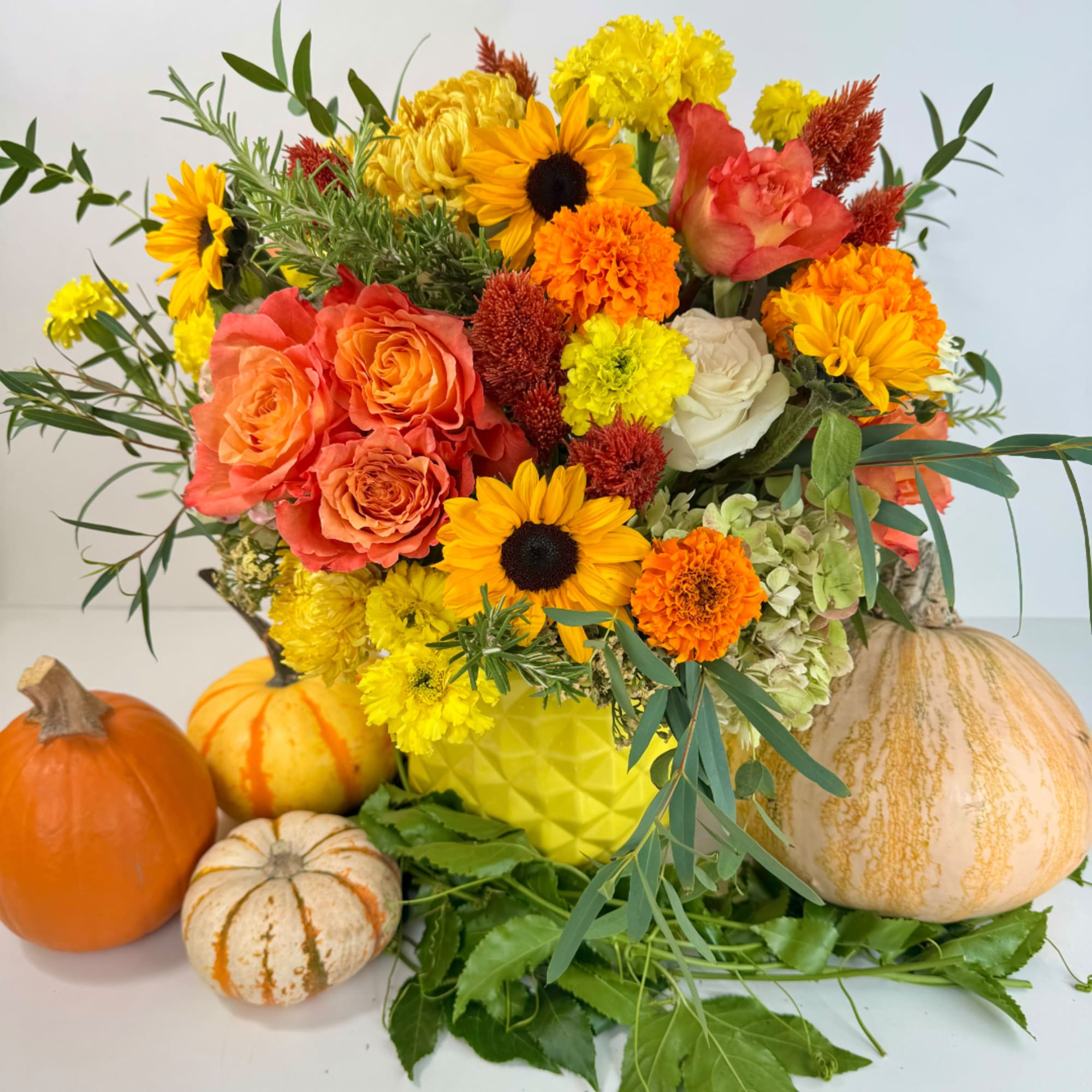 Autumn bouquet with roses, sunflowers, chrysanthemums, and pumpkins in a yellow vase