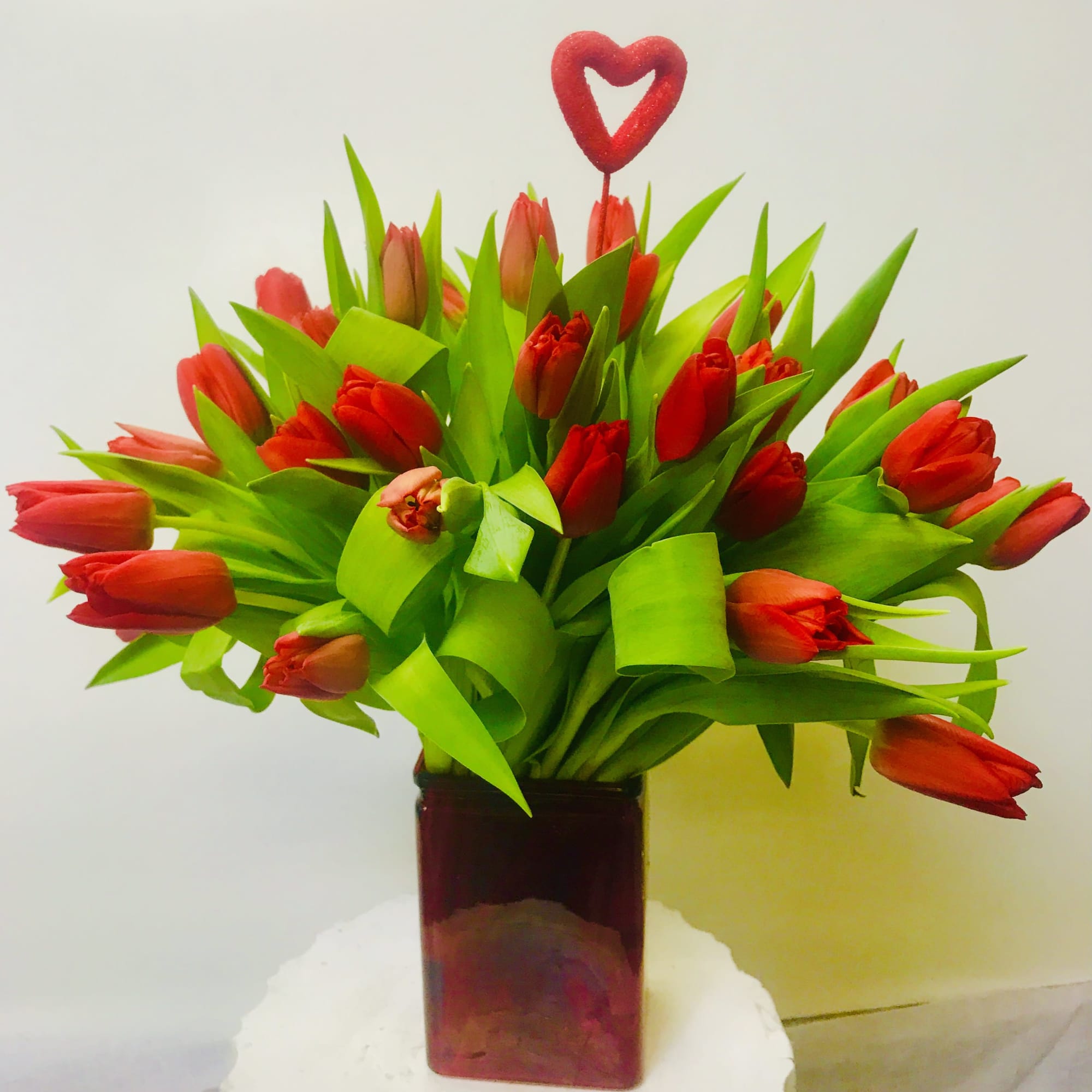 Red tulips arranged in a square vase with a heart pick