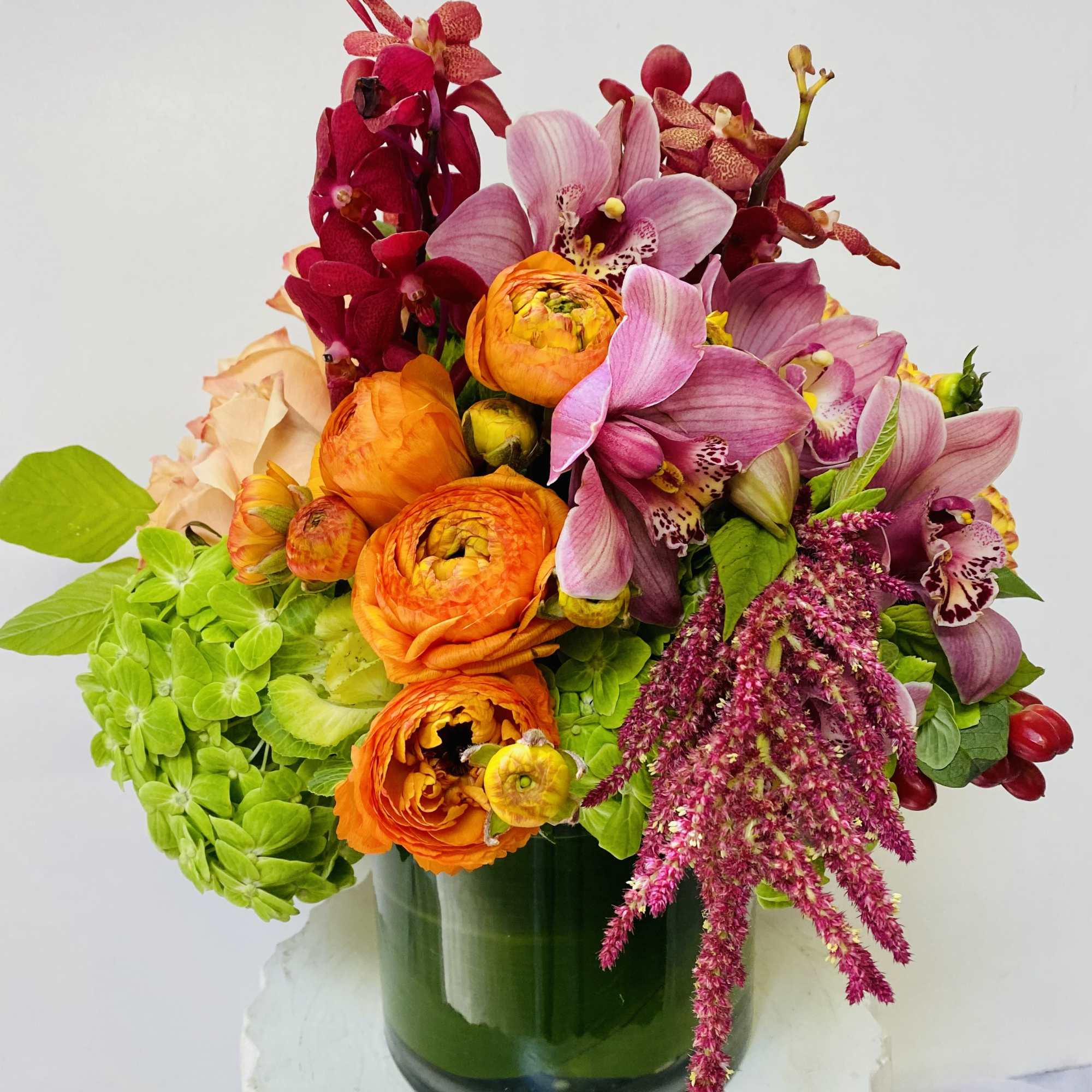 Bright mixed bouquet in a green glass vase with pink orchids and orange blooms