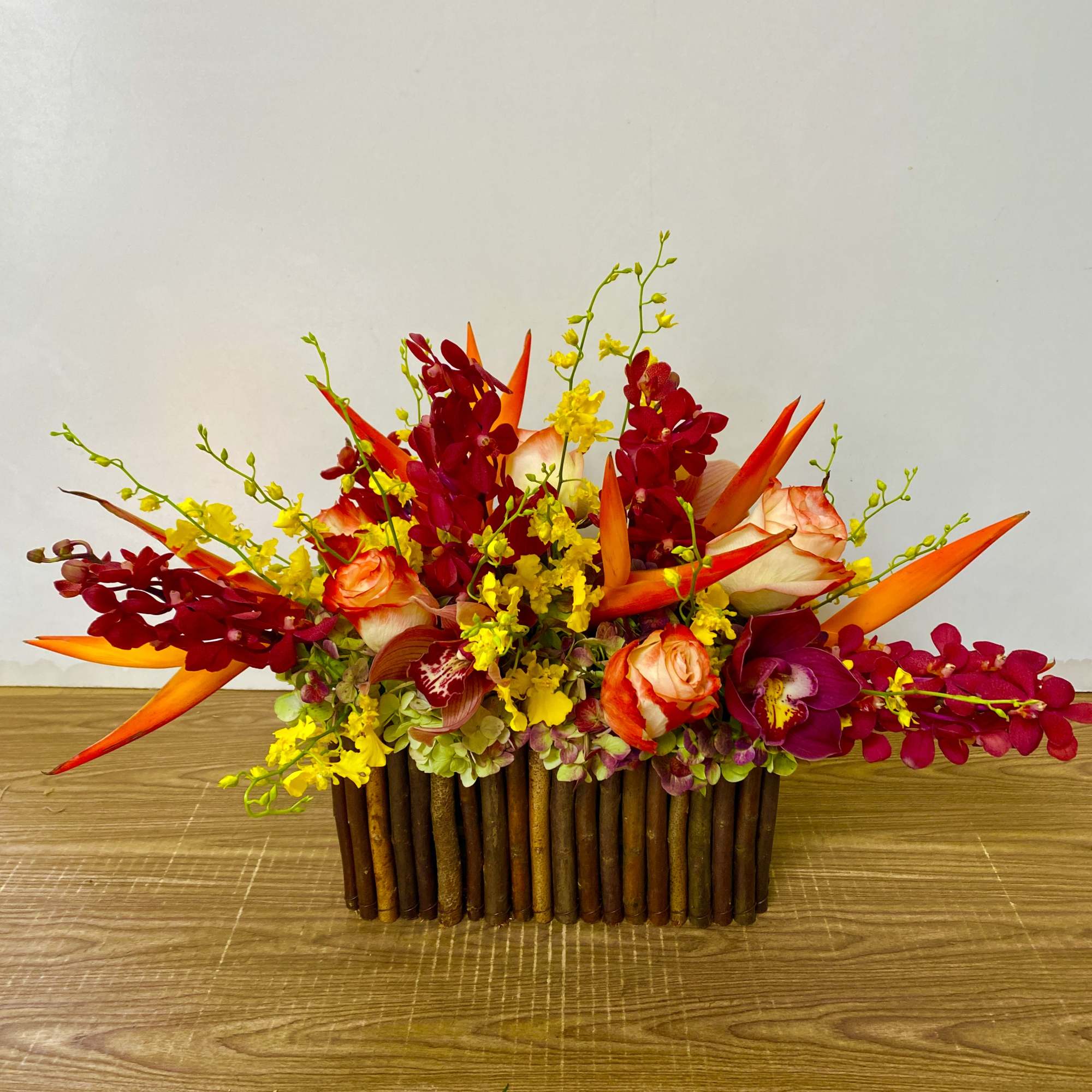 Tropical flower arrangement with orange birds of paradise and red orchids in a wooden container