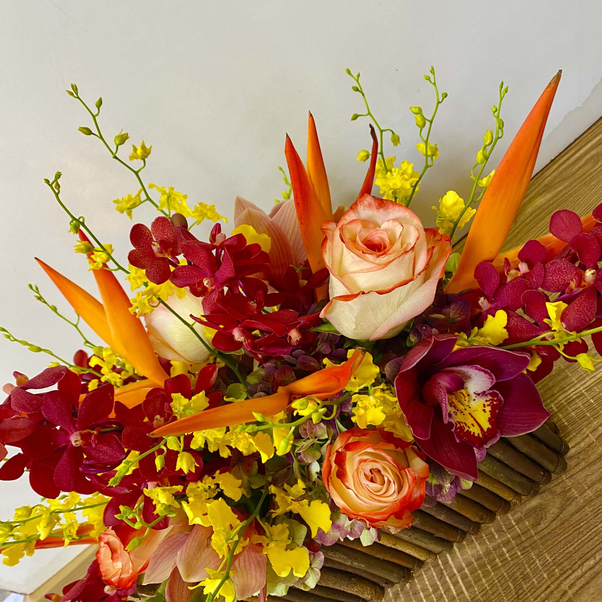 Bright bouquet of orange roses, red orchids, and yellow accents in a wooden container