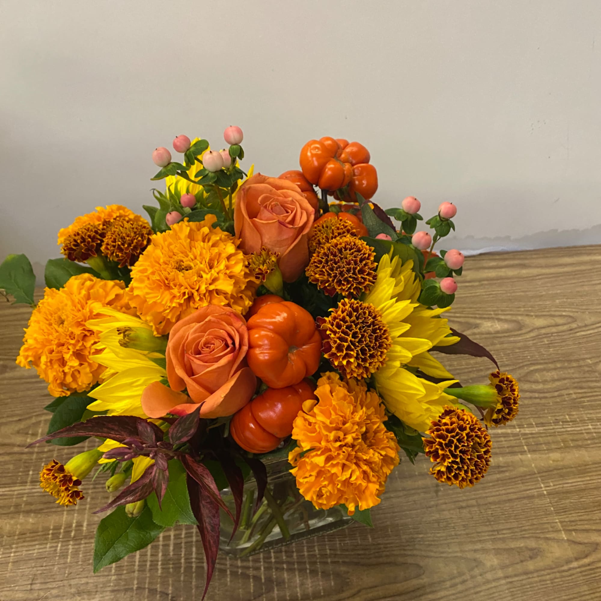 Orange roses and marigolds in a glass vase with yellow sunflowers