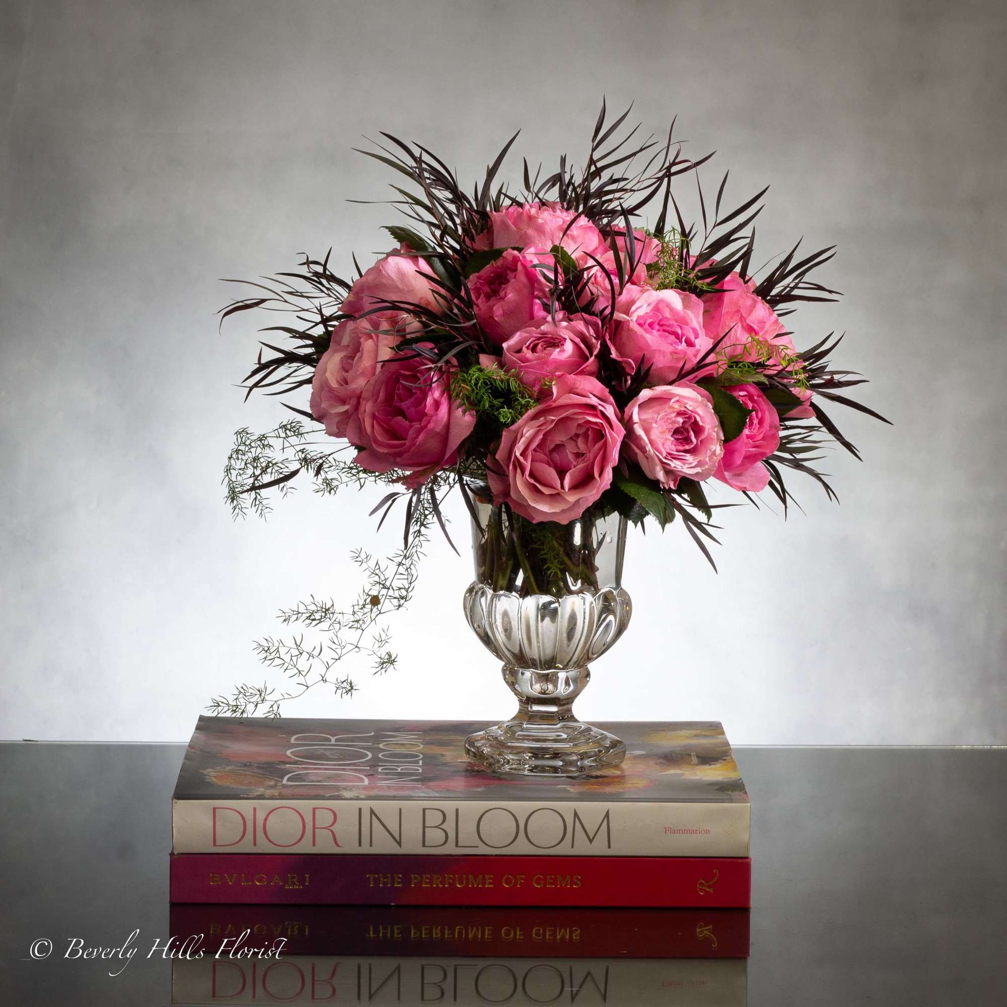 Luscious pink roses with seasonal floral and greens in leaf lined footed