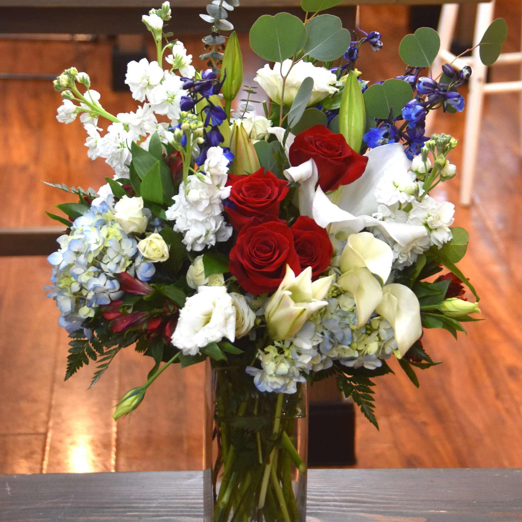 Tall red, white, and blue mixed flower arrangement in a clear rectangular glass vase