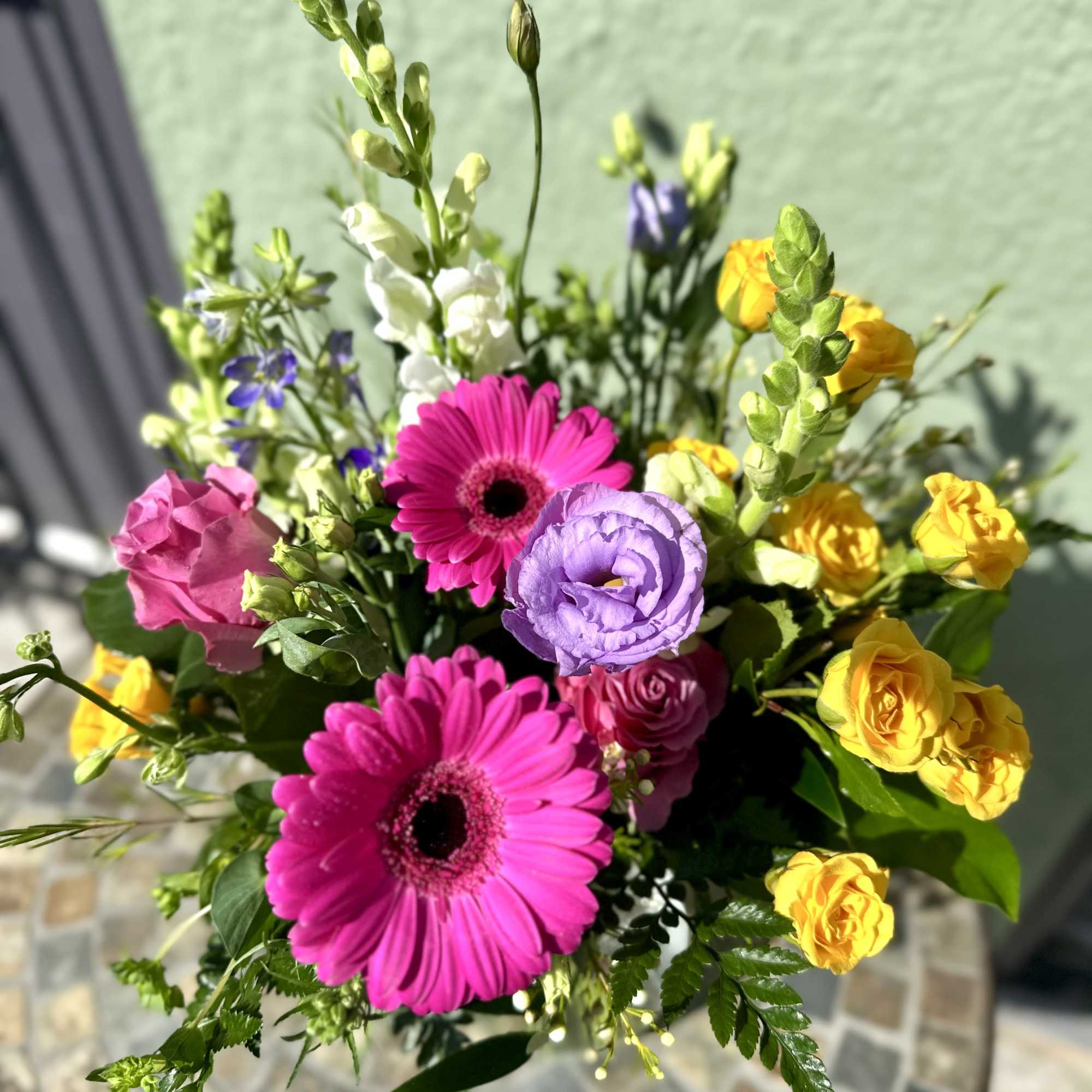 Bright bouquet with hot pink gerbera daisies, yellow spray roses, purple lisianthus, and white snapdragons