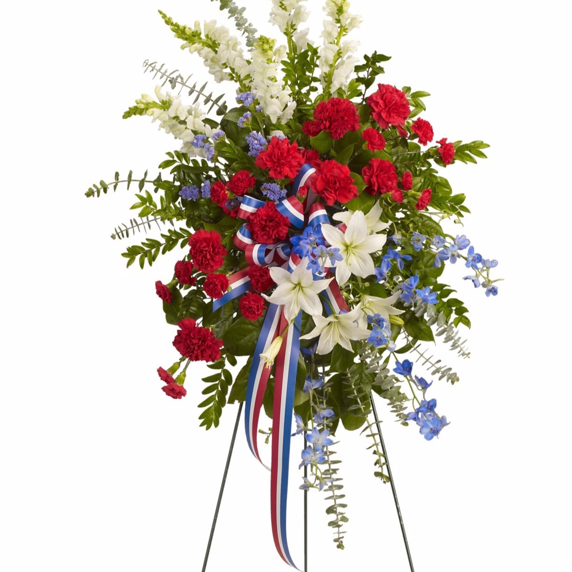 Patriotic standing spray with red carnations, white lilies and blue flowers on an easel with a tricolor ribbon.