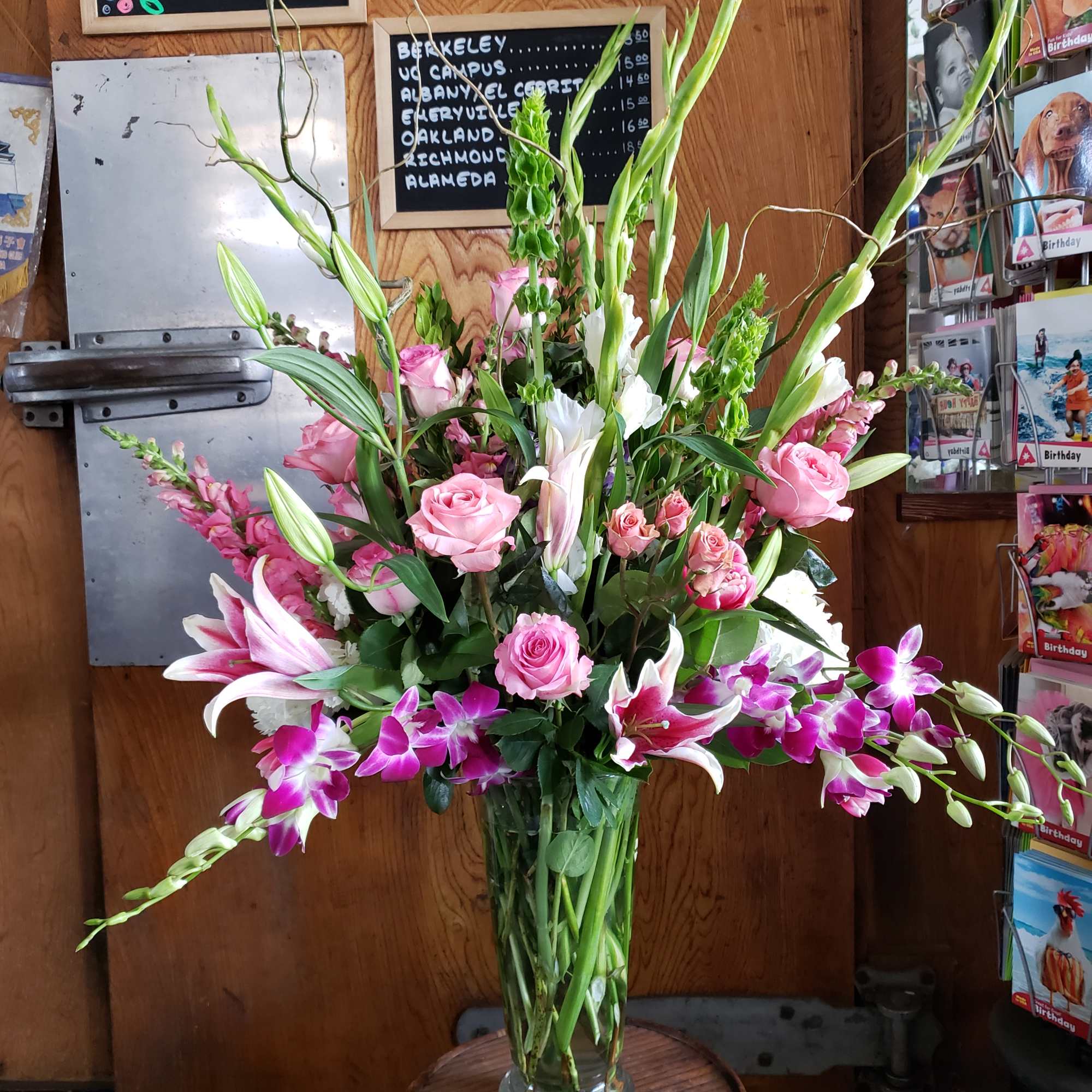 Tall bouquet of pink roses, lilies, and purple orchids in a glass vase
