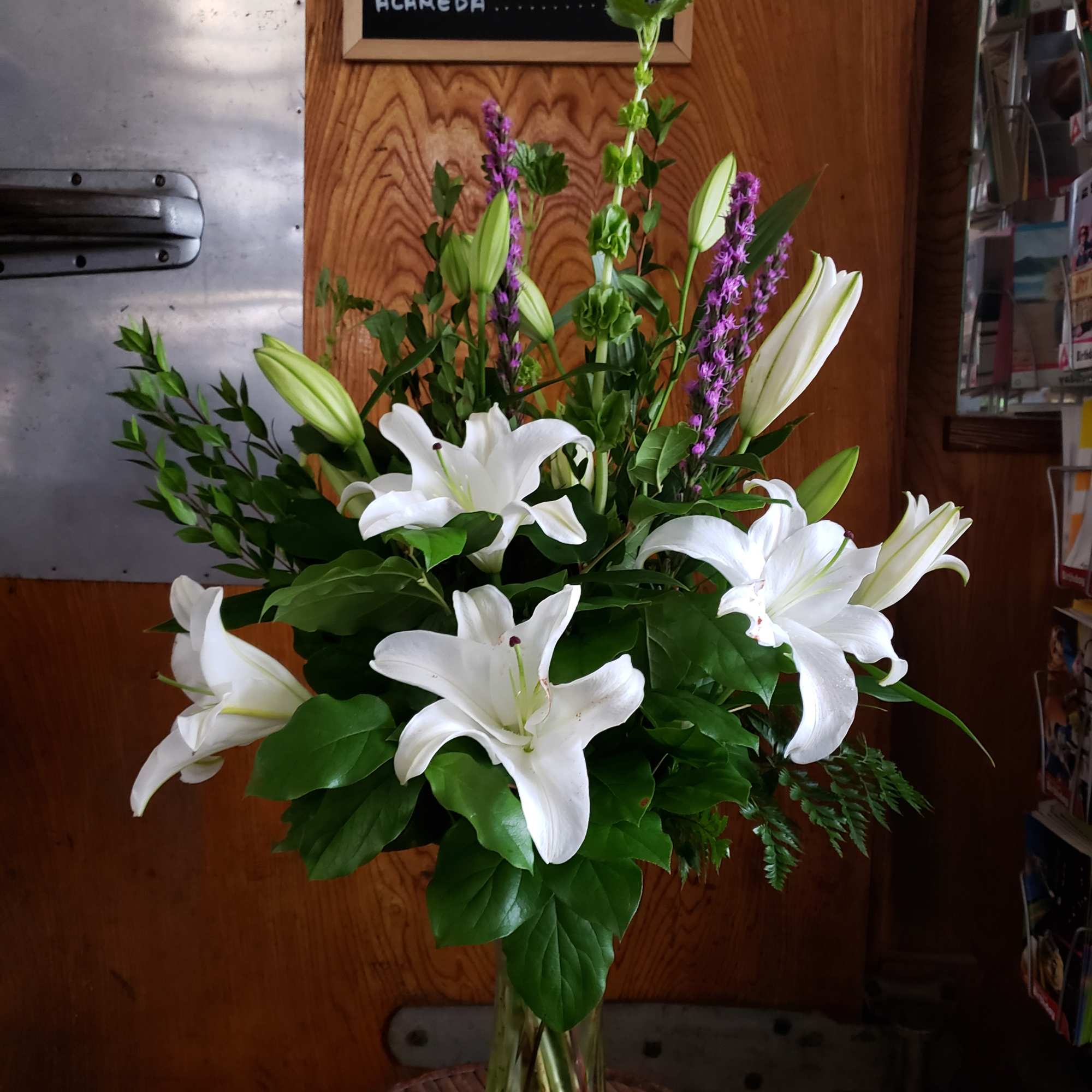 Tall bouquet of white lilies and purple spikes in a glass vase