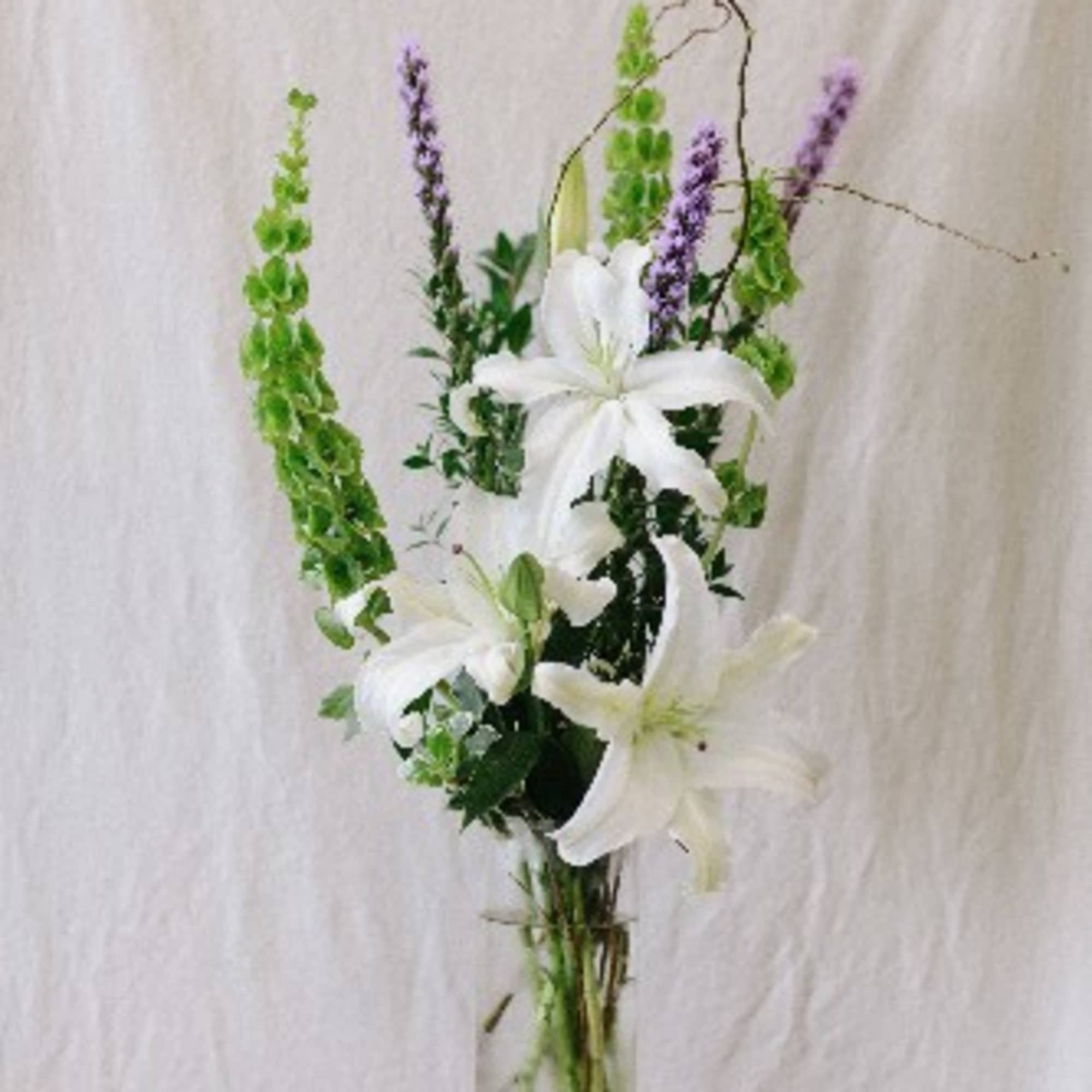 Tall white lily arrangement with green and purple spikes in a glass vase