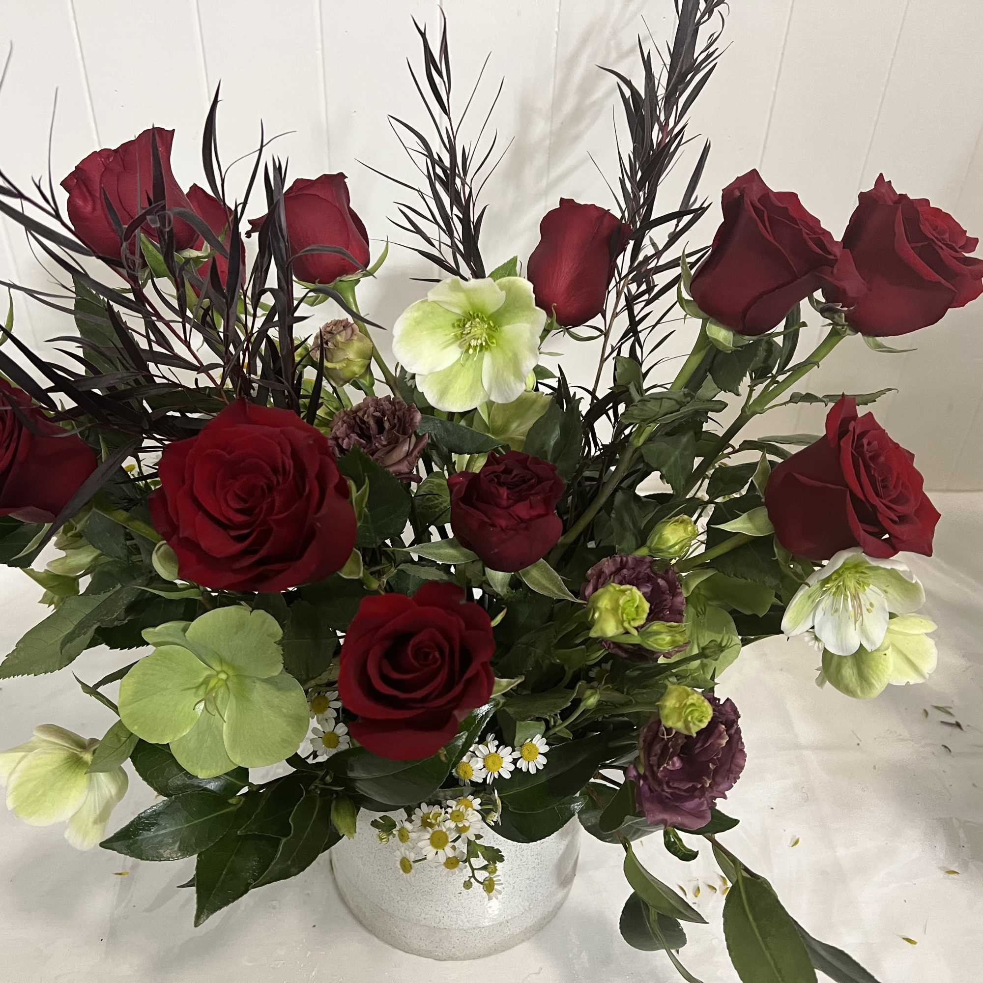 Red roses and pale green-white blooms in a white vase