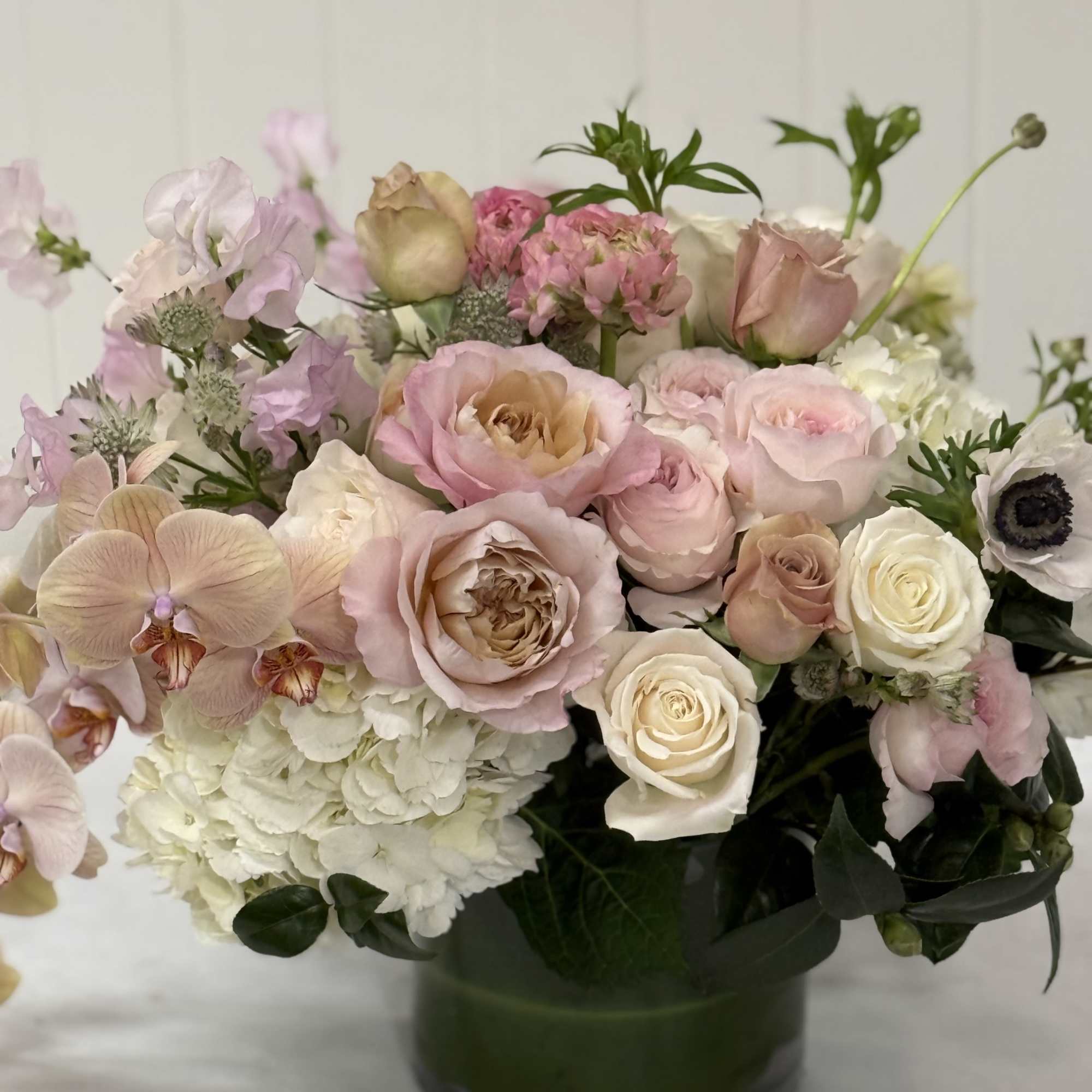 Pink and white roses with orchids and hydrangea in a glass vase