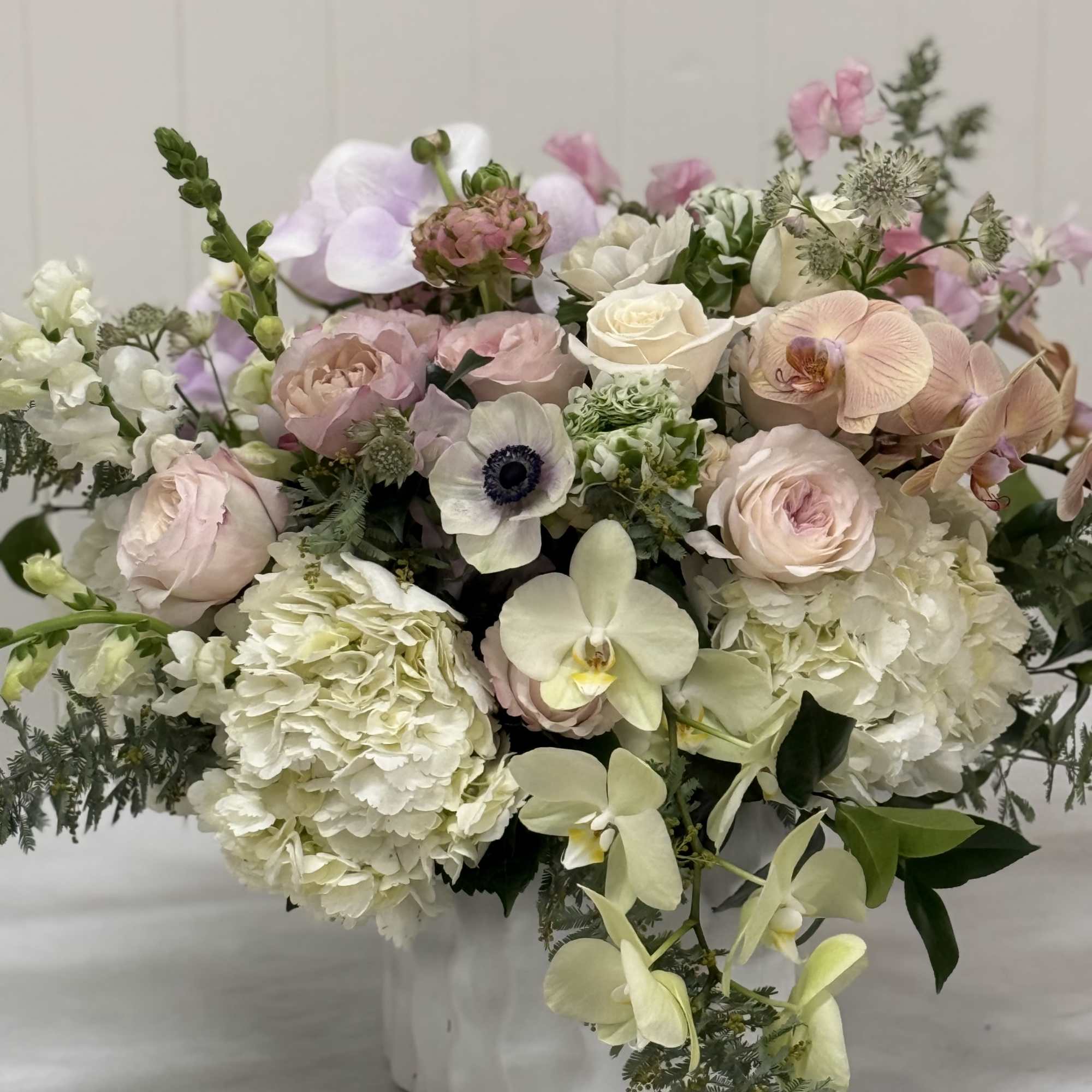 Pastel bouquet with roses, hydrangeas, orchids, and anemones in a white vase