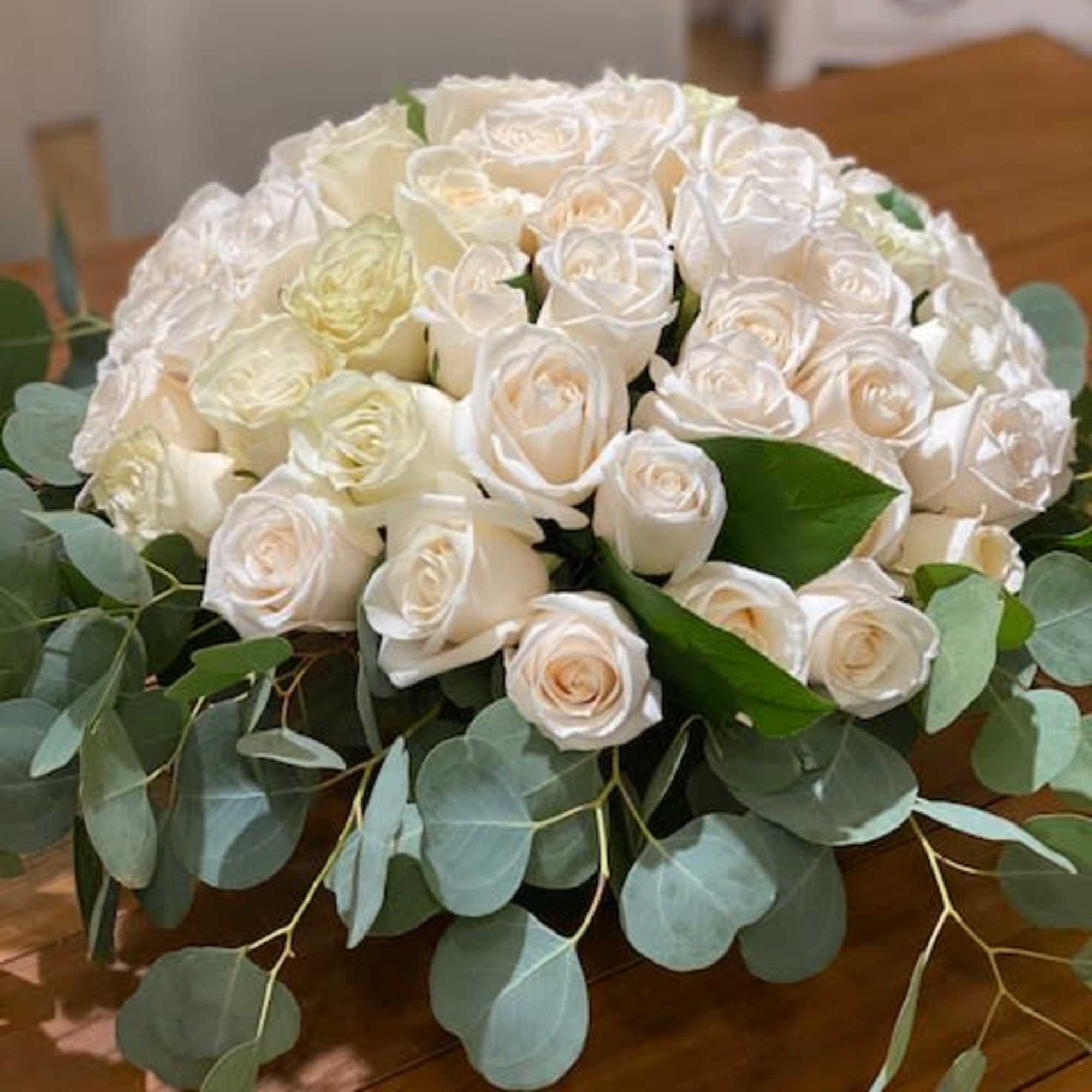 Low centerpiece of ivory roses surrounded by silver-green eucalyptus on a wooden table