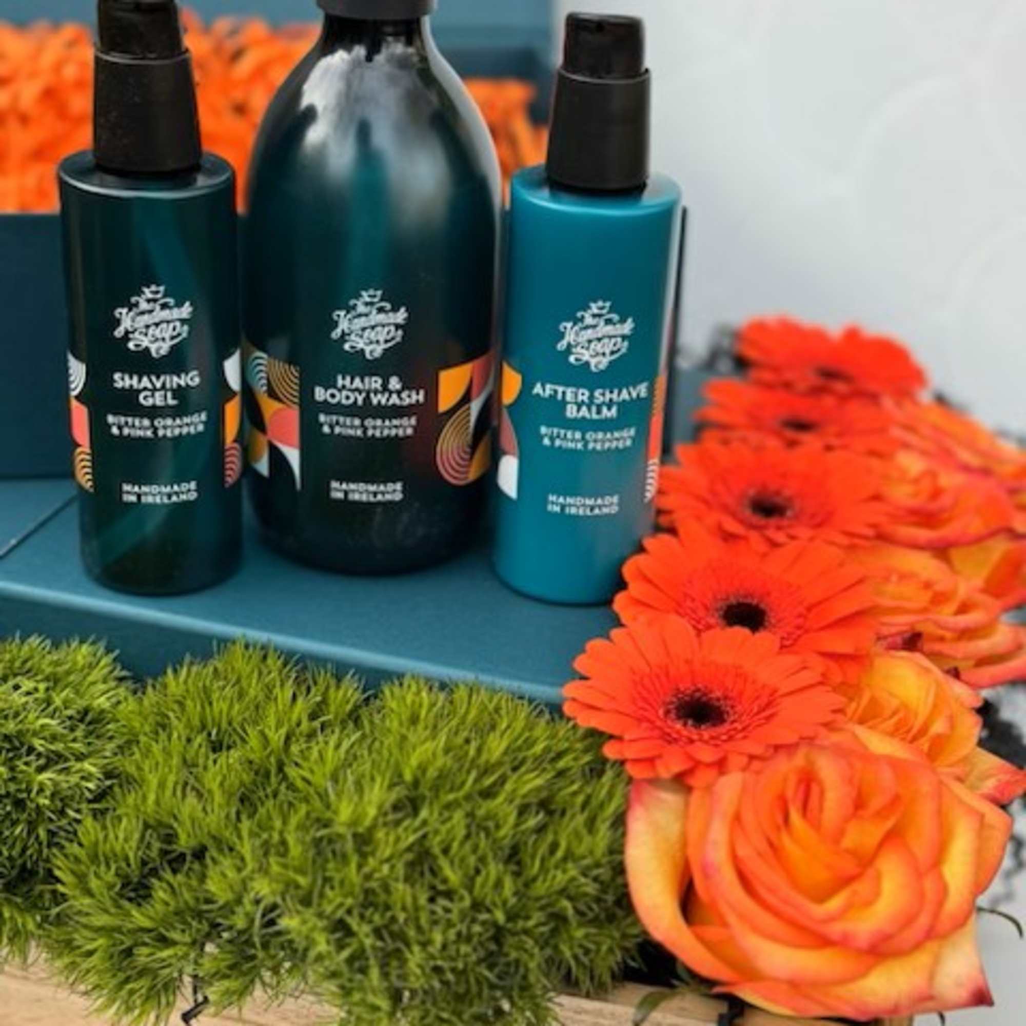 Teal grooming gift set with orange roses and gerbera daisies in a wooden tray.