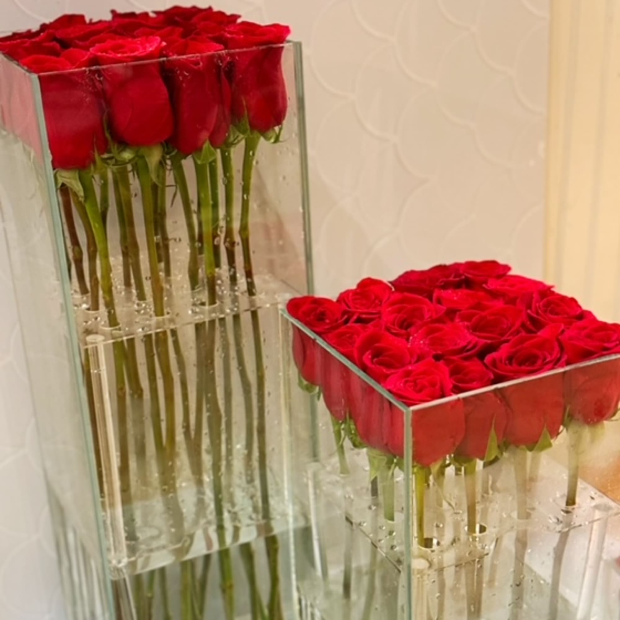 Two clear glass vases filled with tightly packed red roses.