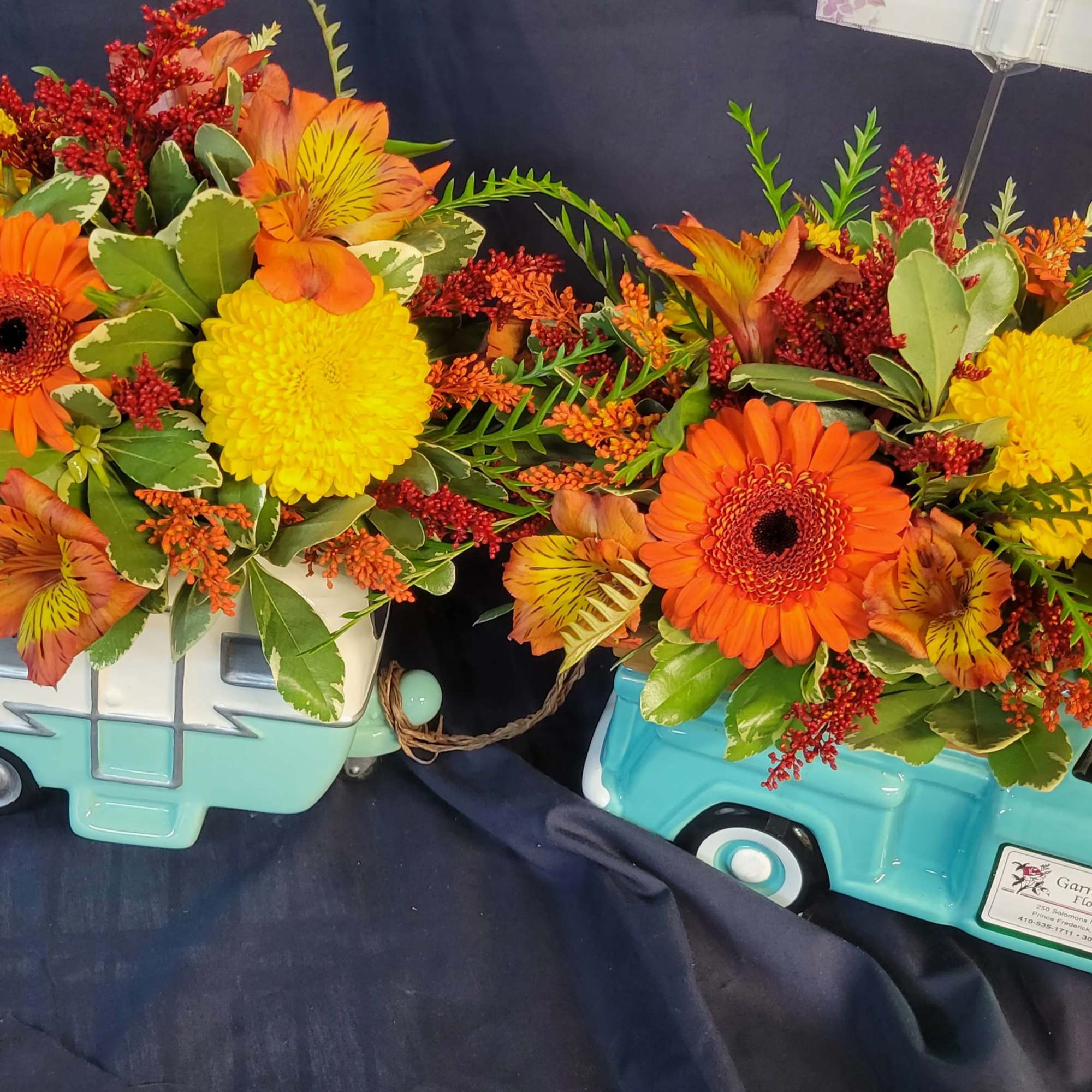 Two floral arrangements in turquoise truck containers with orange and yellow blooms, photo 3 of 3