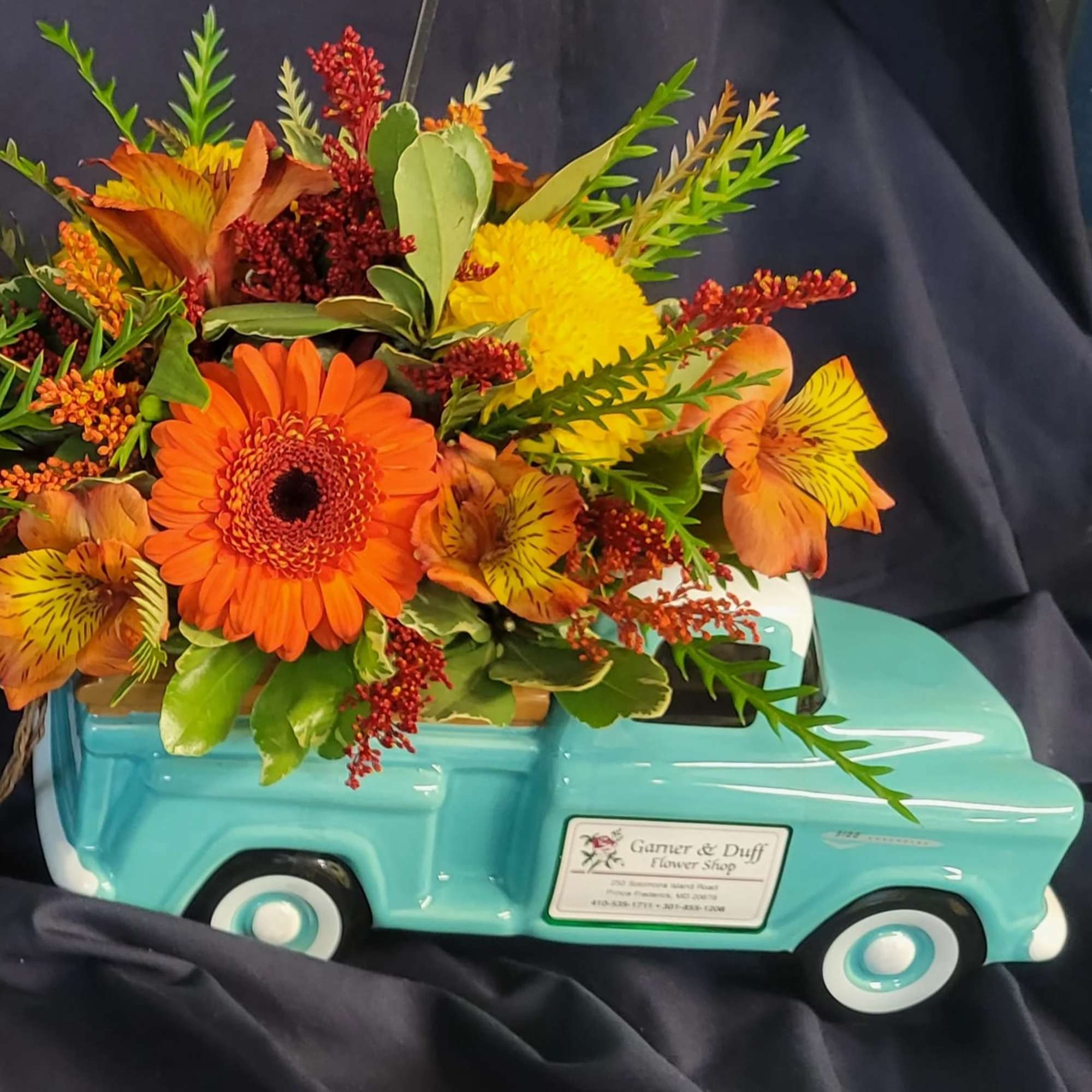 Orange and yellow flowers arranged in a turquoise truck-shaped container