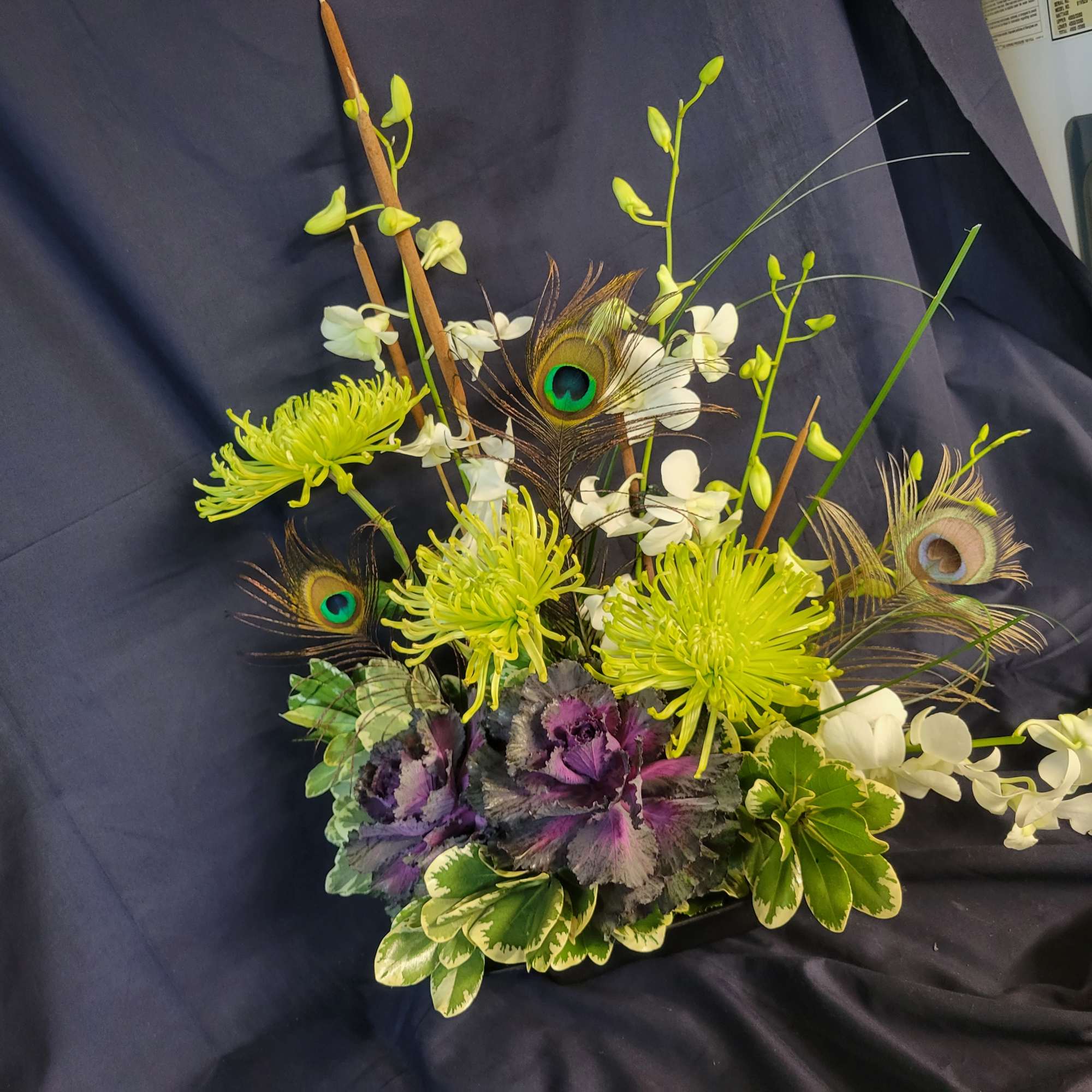 Arrangement of green spider mums, white orchids, and peacock feathers