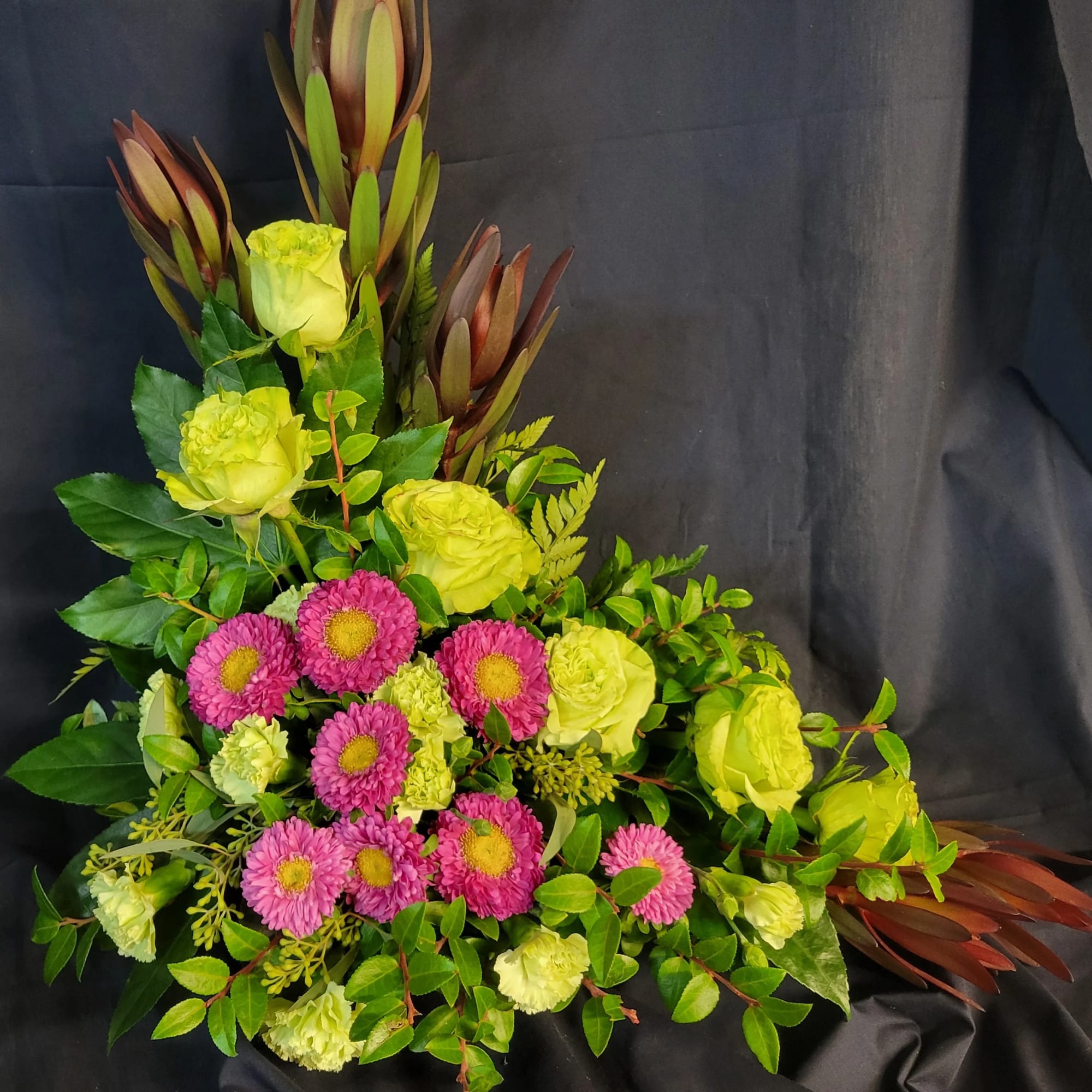Bouquet of lime roses and pink daisies with tall tropical foliage