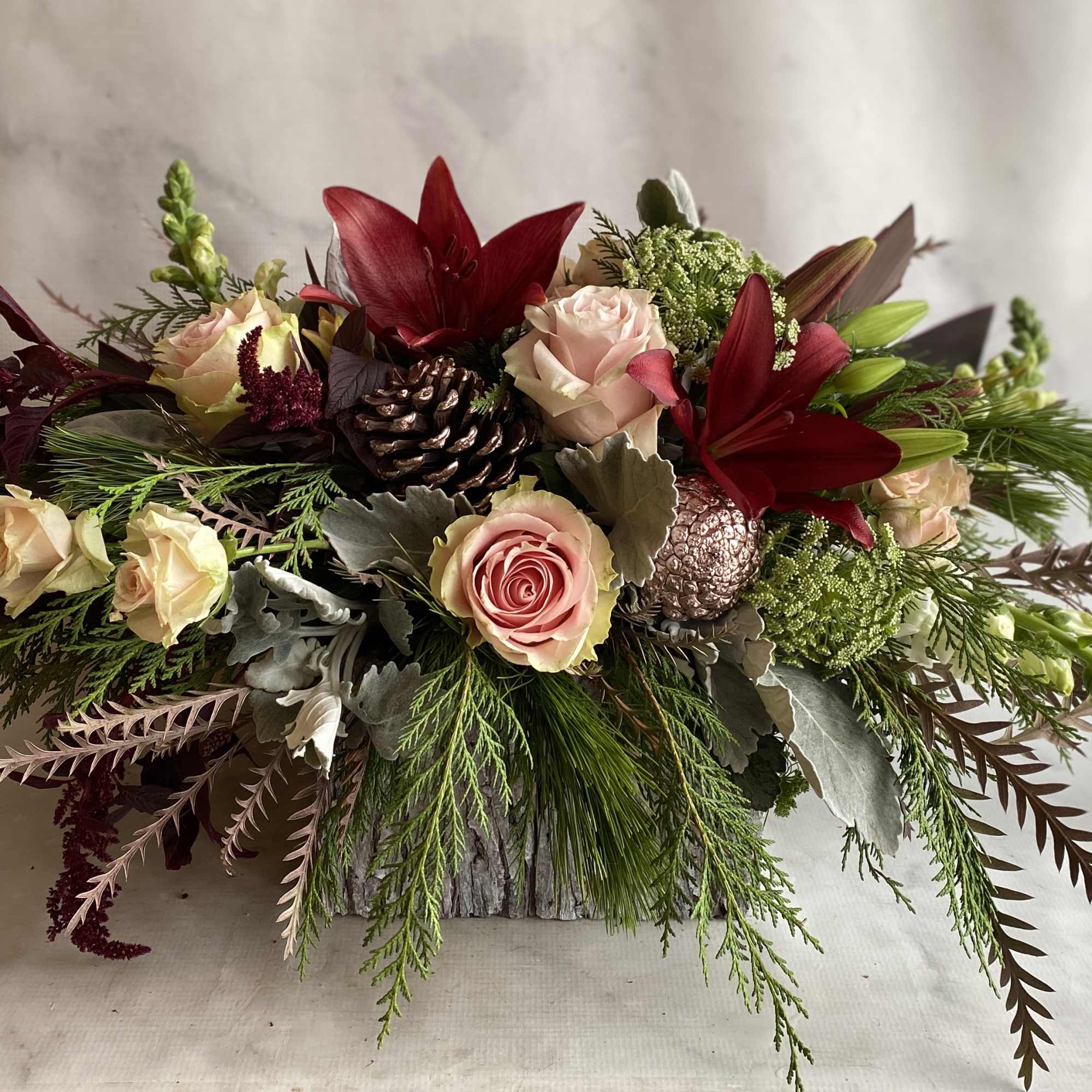 Roses, snap dragons, red lilies, pine cones, Xmas greenery and hanging amaranthus